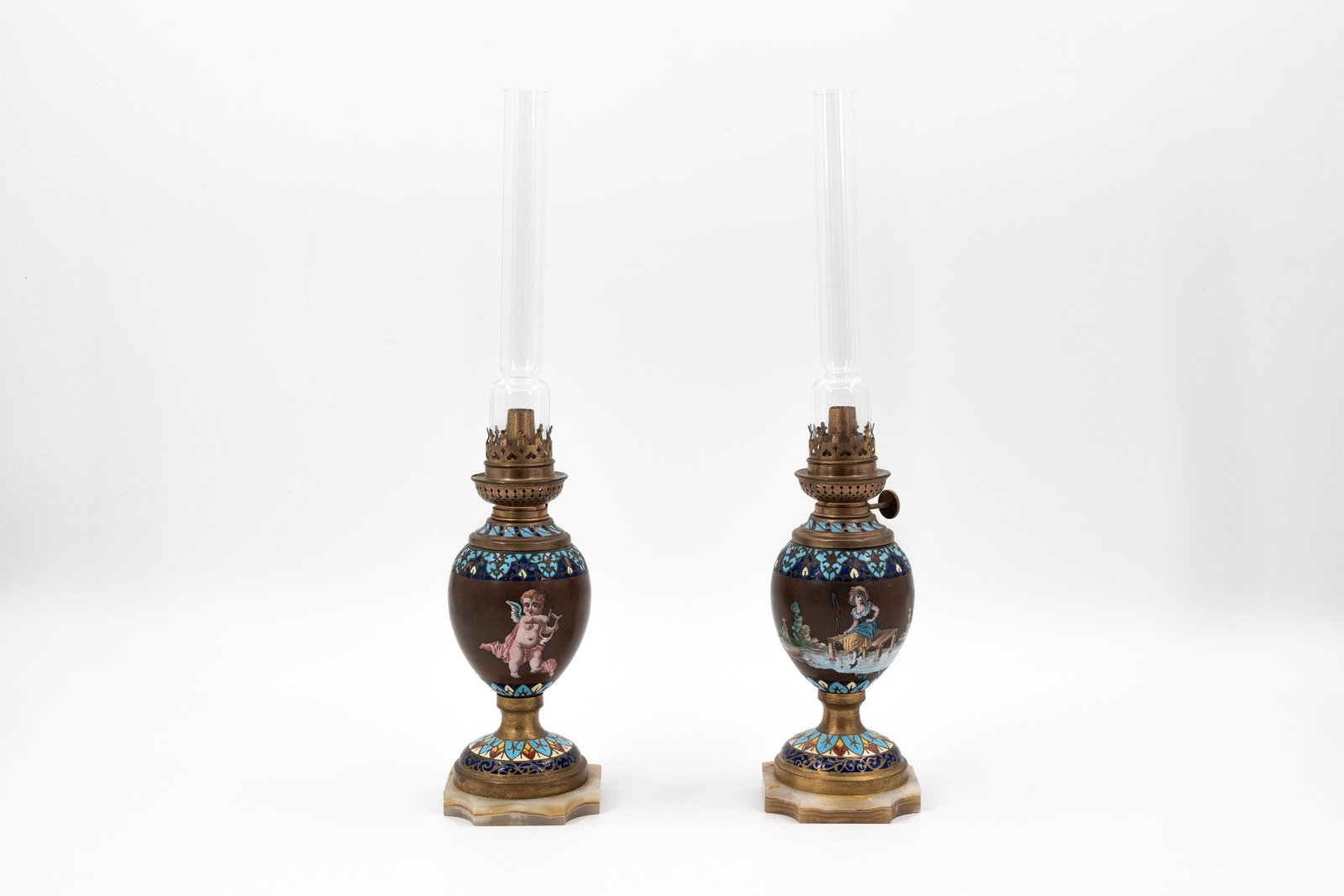 A pair of antique champleve and brass mounted oil lamps: A pair of antique champleve and brass mounted oil lamps, decorated with enamel scene of children. Mounted on an onyx marble base. Circa 1900. H: 43 cm