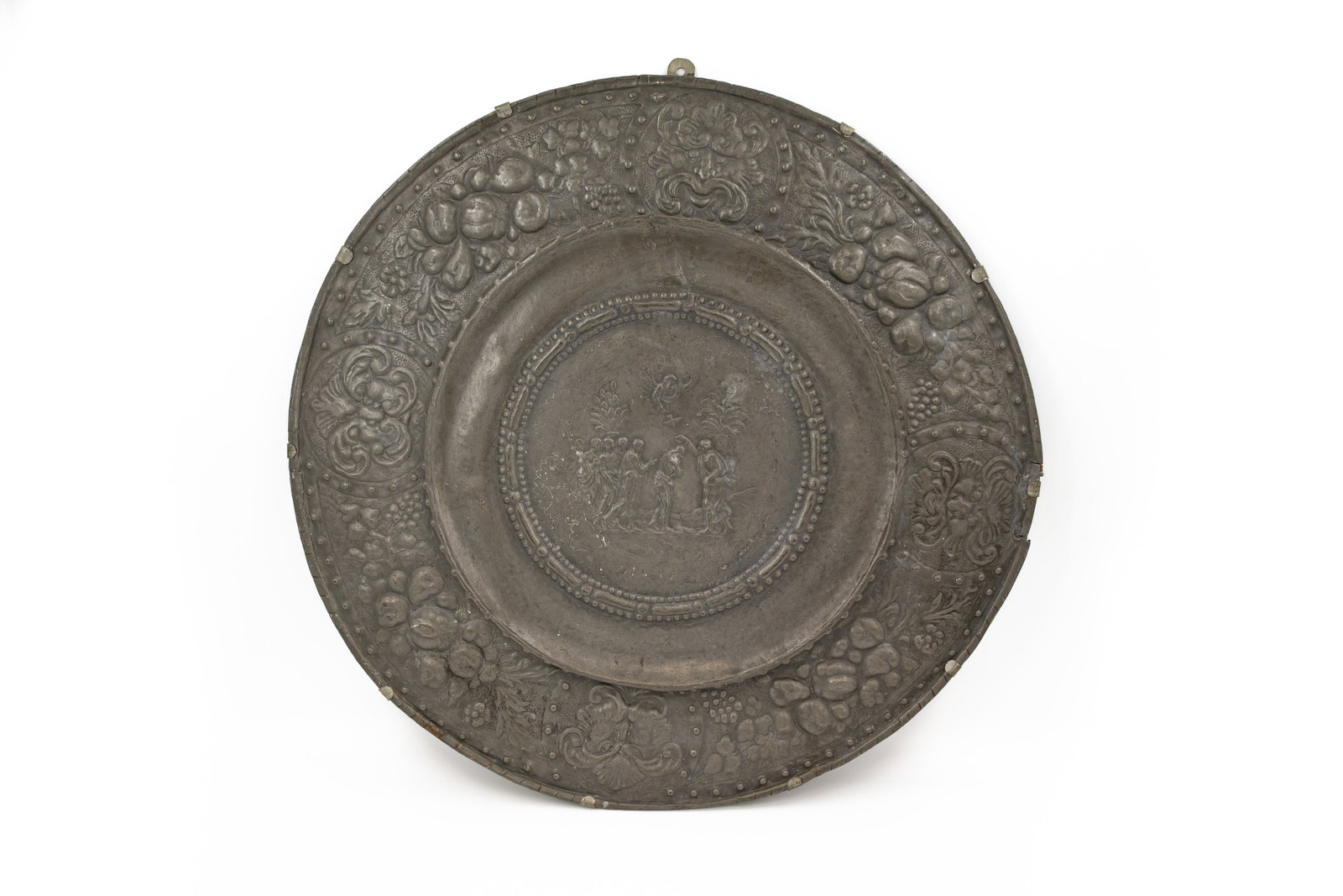 A large and antique bas reliëf decorated repoussé pewter round wall plate with figural scene: A large and antique bas reliëf decorated repoussé pewter round wall plate with figural scene and fruit decorated rim. 18th/19th century. W: 75 cm