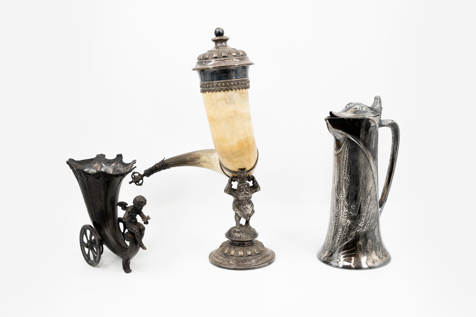 A composed lot of three variously shaped silver plated objects: A composed lot of three variously shaped silver plated objects. Consisting of: one horn shaped vase on wheels with putti, one probably with pewter mounted buffalo horn with a figure and one silver pla