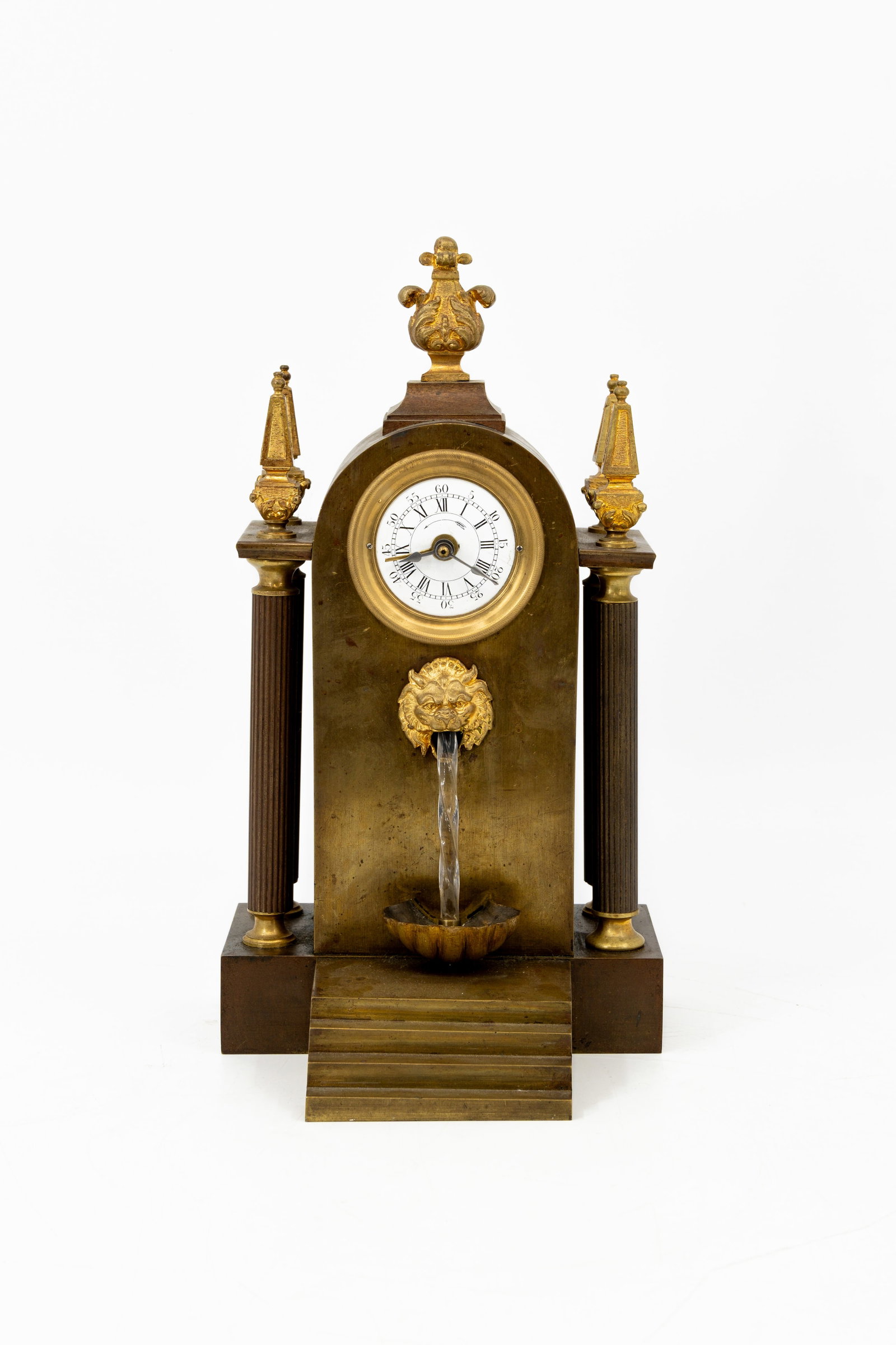 An antique gilt and patinated bronze automaton fountain table clock: An antique gilt and patinated bronze automaton table clock with movable glass fountain. Late 19th century. H: 33 cm