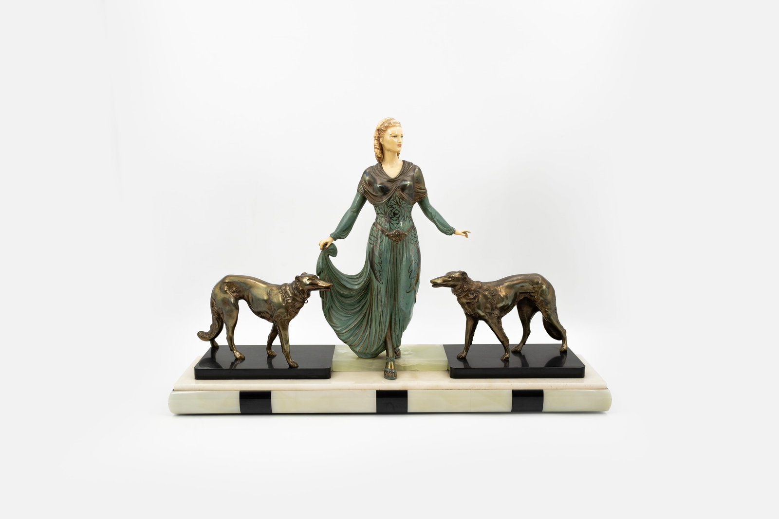An art deco patinated spelter and resin figural sculpture group: An art deco patinated spelter and ivorine sculpture group of a lady with two greyhounds. Mounted on a multi-color marble base. H: 50 - W: 74 cm