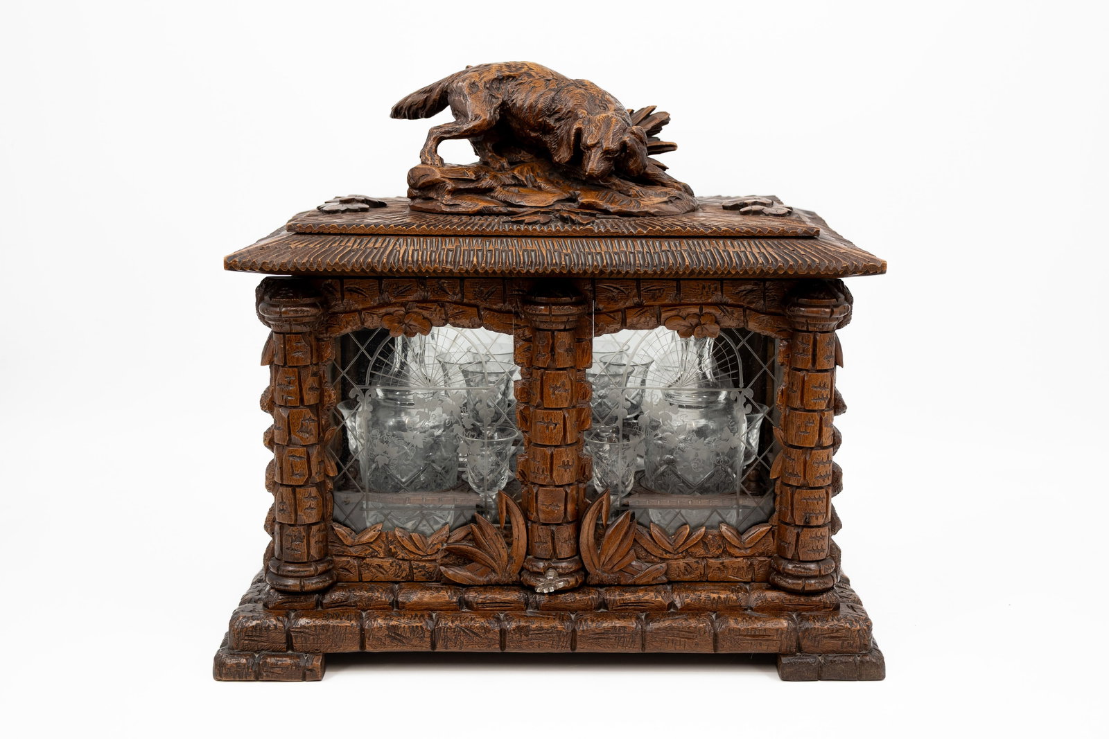 A richly carved wooden Black Forest liqueur cabinet: A richly carved wooden Black Forest liqueur cabinet decorated with a hunting dog and cut glass. Inside filled with four cut glass decanters with matching glasses. Circa 1900. H: 39 - W: 44 - D: 31 cm