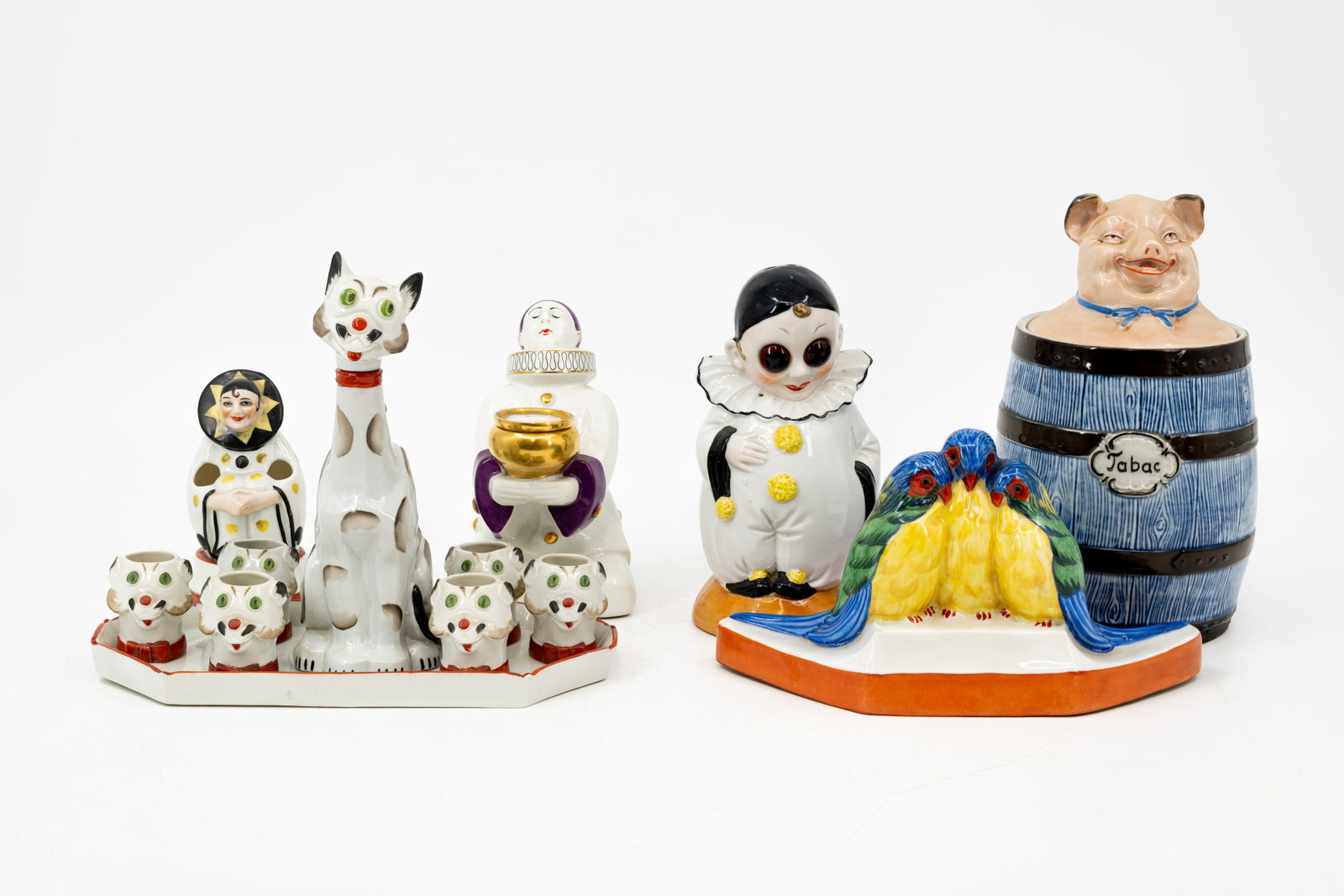 An antique composed lot of variuos art deco porcelain items: A composed lot of various antique art deco porcelain items. Consisting of: - one tobacco jar - one trinket tray - three clown figurines - one cat-shaped drinking set. Various marks, Limoges, and numbe
