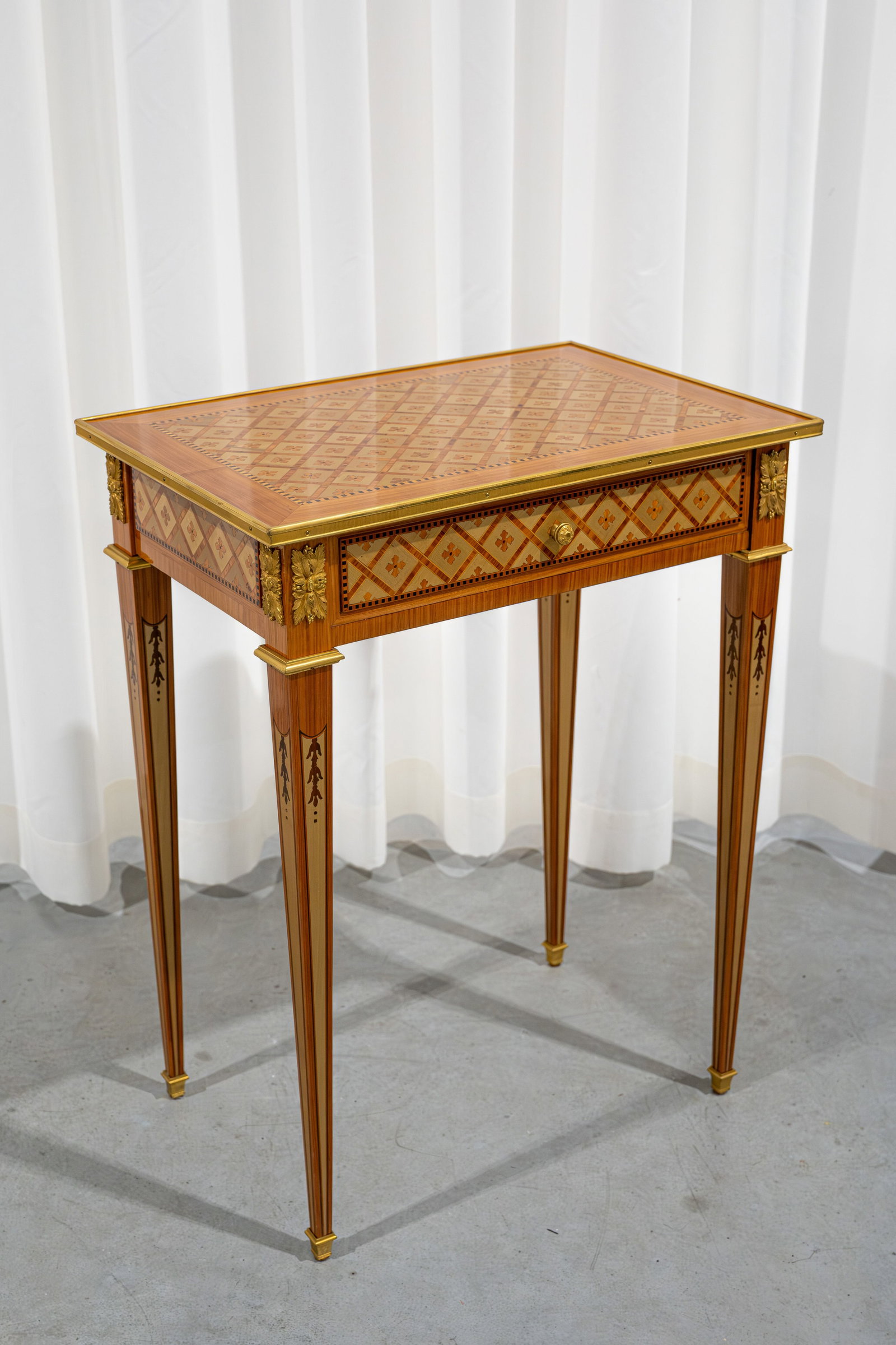A 20th century Louis XVI-style wooden side table with a drawer, decorated with marquetry inlay: A 20th century Louis XVI-style wood side table with a drawer finely decorated with marquetry inlay tulip and gilt bronze mountings. Circa 1980s. H: 68 - W: 53 - D: 36 cm