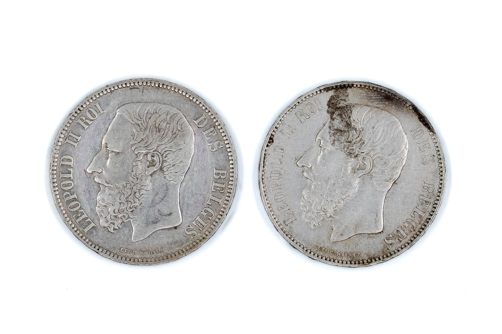 A lot of two Belgian silver 5 Francs coins (Leopold II), dated 1868-1874: A lot of two Belgian silver 5 Francs coins (Leopold II), dated 1868-1874. Comprising 5 Francs 1868 and 5 Francs 1874, with crowned coat of arms within wreath on reverse. Weight: 25 - 25g