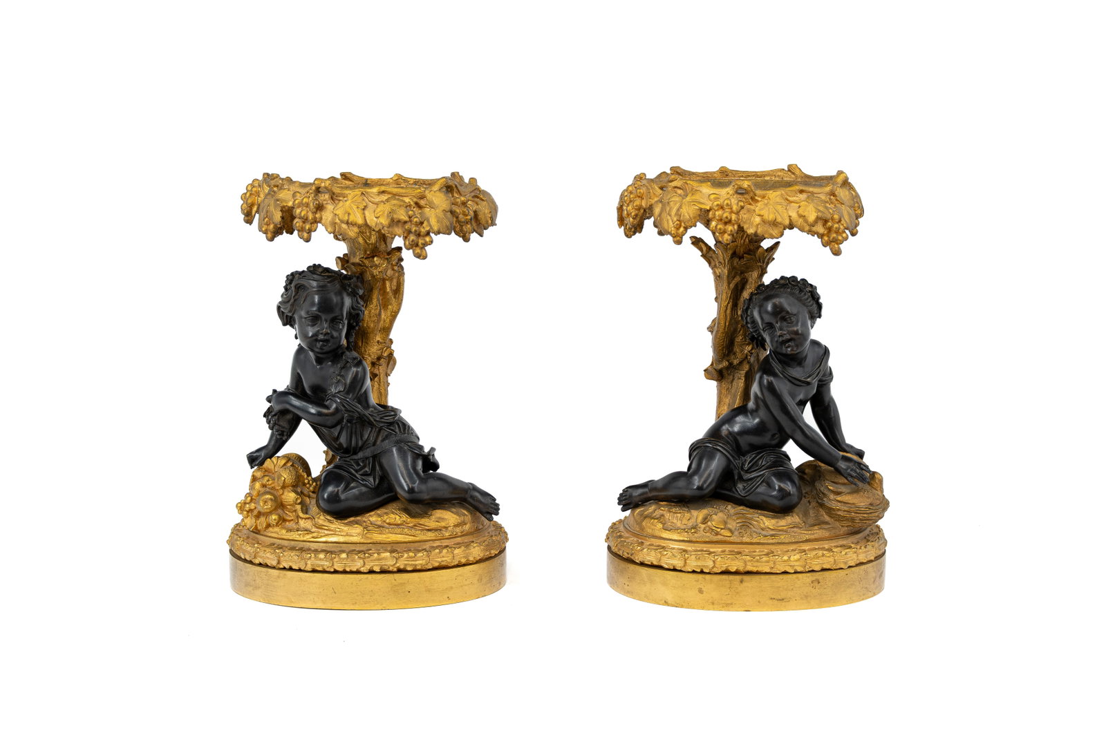A pair of antique French Rococo-style gilt and patinated bronze figural tazze: A pair of antique French Rococo-style gilt and patinated bronze figural tazze, decorated with seated putti and Bacchic motifs of grapes and vine leaves, in the manner of Clodion. 19th century. H: 31 c