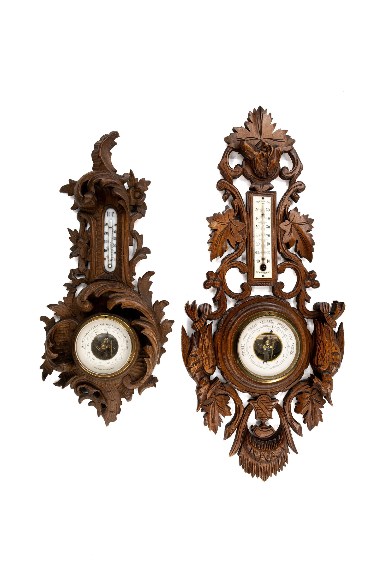 A composed lot of two antique German Black forest carved wooden weather stations: A composed lot of two antique German Black forest carved wooden weather stations, variously decorated with hunting and floral motifs. 19th/20th century. H: 54 - W: 25 cm H: 72 - W: 32 cm