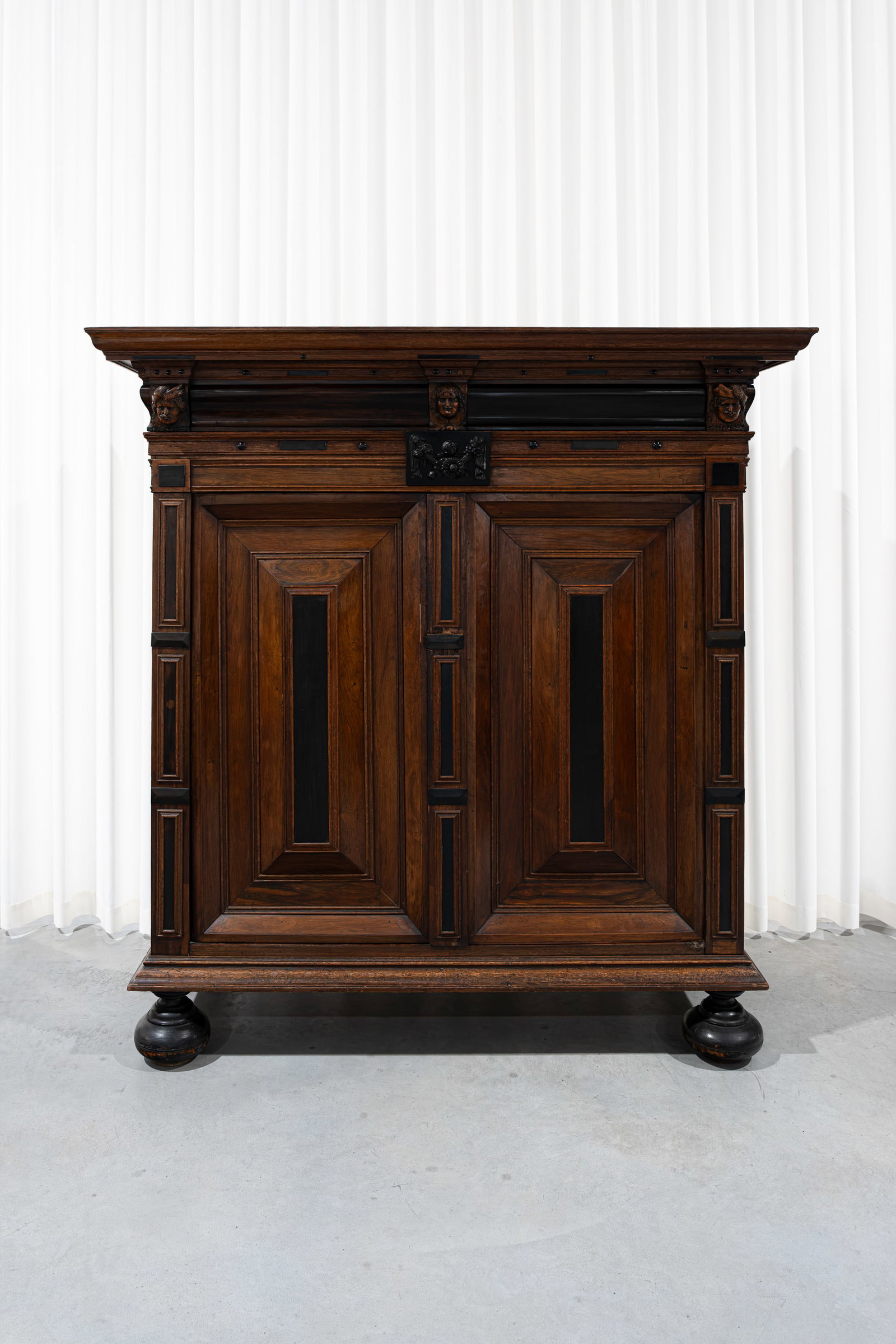 An antique Dutch pillow cabinet with blackened and walnut veneer: An antique Dutch pillow cabinet with blackened and walnut veneer and decorated carved head figures. 17th/18th century. H: 182 - W: 175 cm