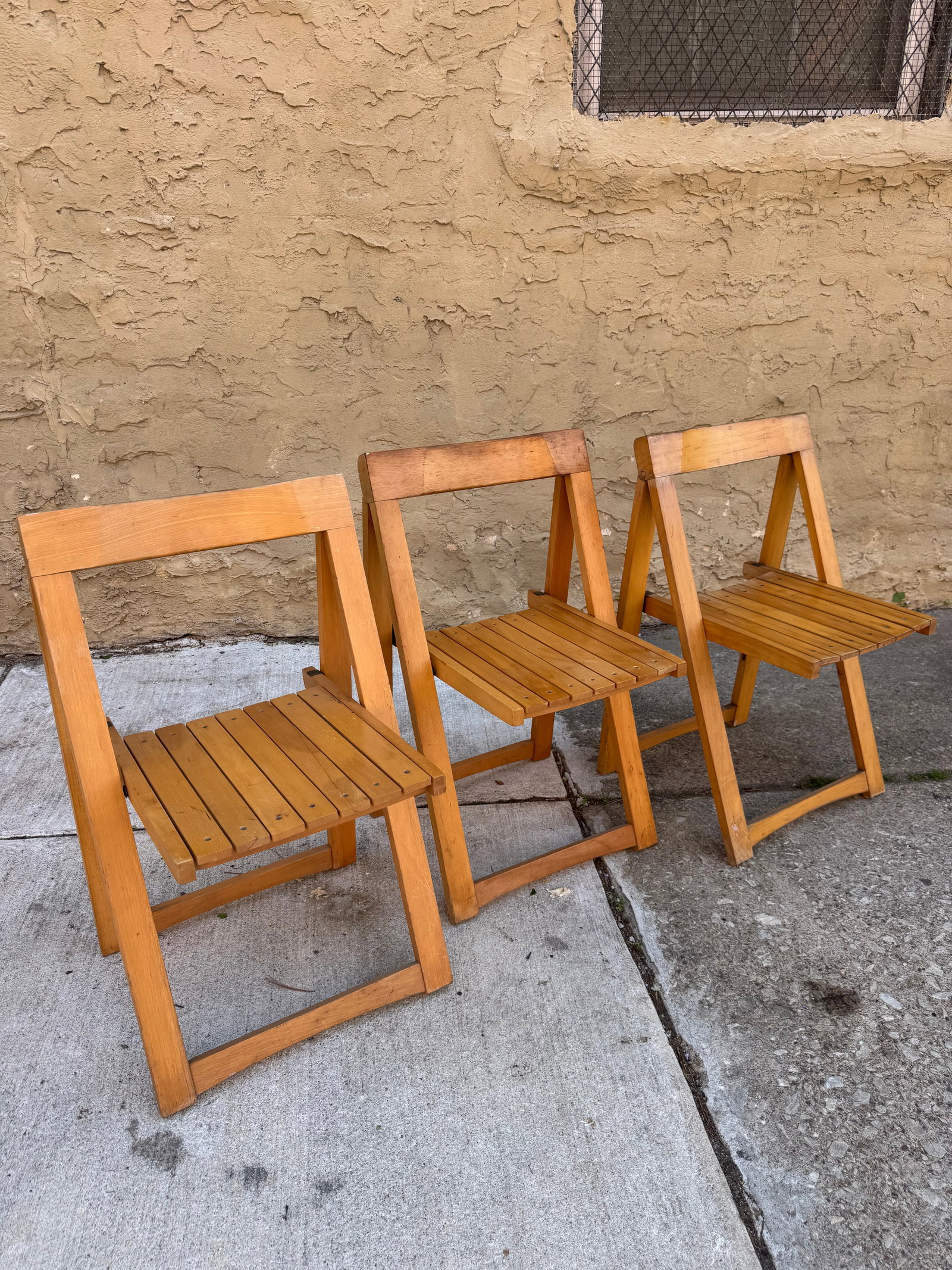 Lot of 3 Vintage Mid-Century Style Folding Chairs: Set of three vintage mid-century modern folding chairs in the iconic “Trieste” style by Aldo Jacober, featuring sculptural geometric frames and slatted blonde wood construction. Their minimali