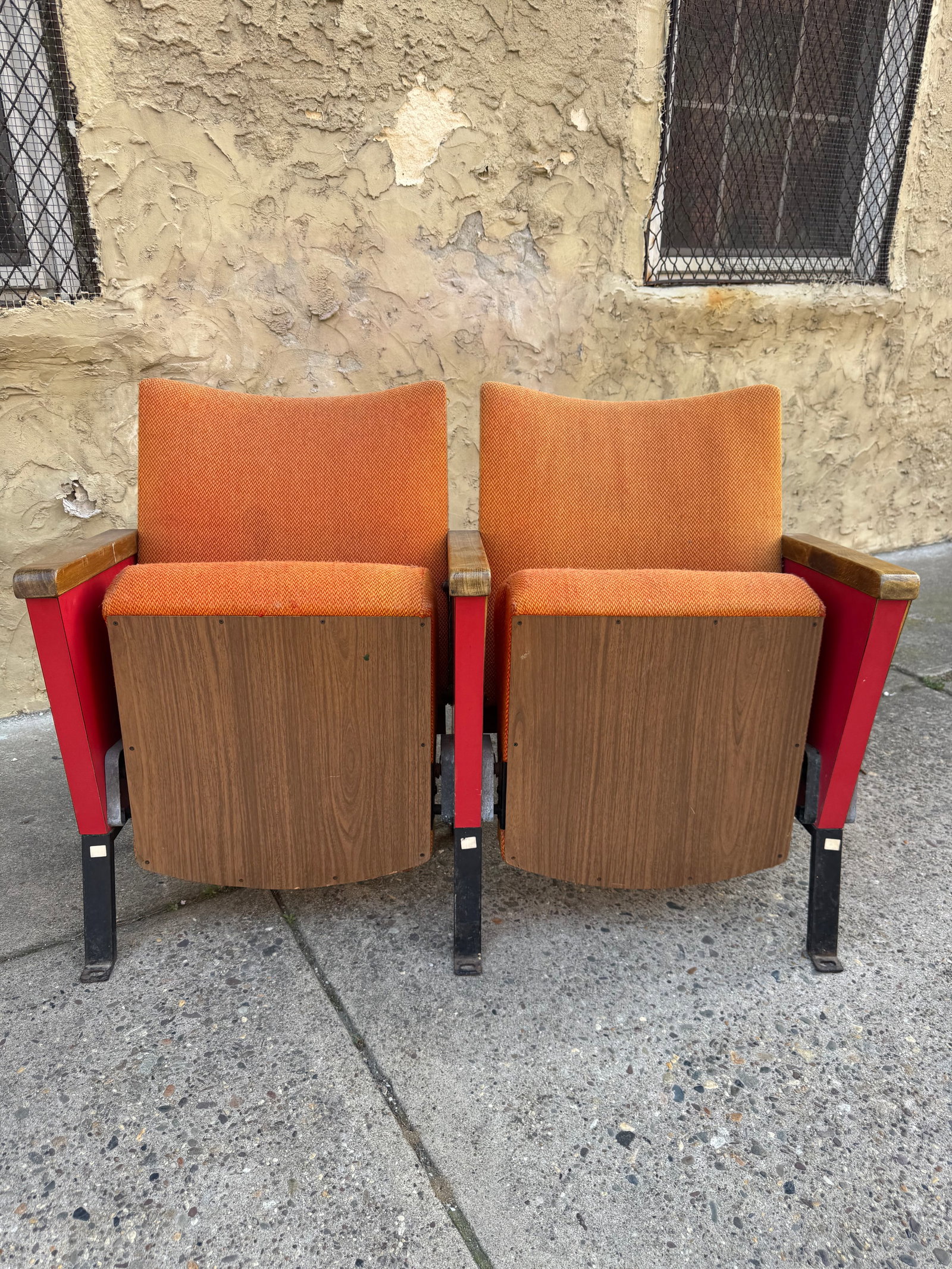 Vintage Mid-Century Modern Auditorium Theater Seats – Pair, Orange & Red Industrial Seating: Rare pair of authentic mid-century modern auditorium seats featuring original orange upholstery, crimson metal side panels, and black iron frames with folding seat mechanisms. Richly patinated wood ar