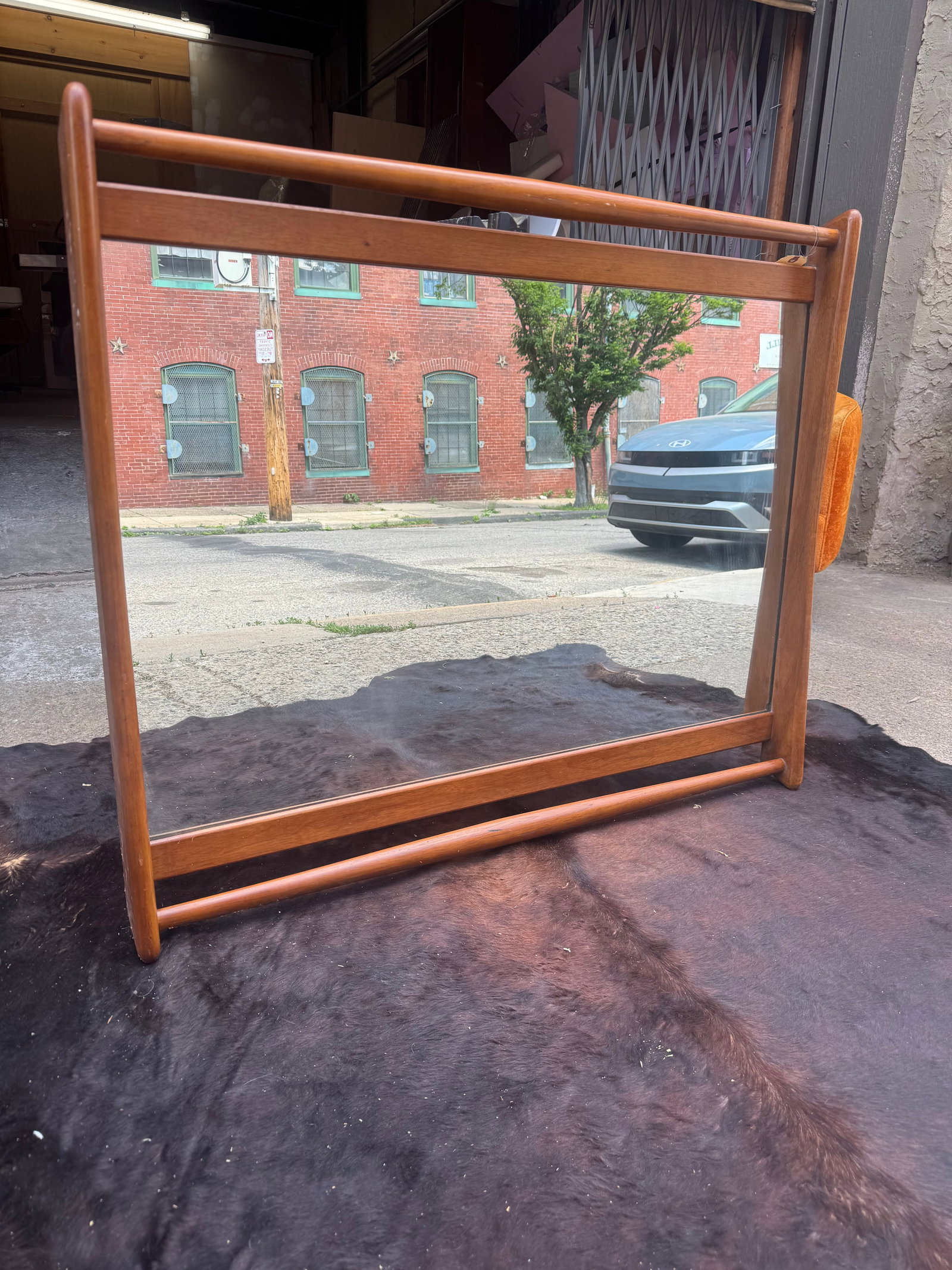 Mid-Century Modern Wood Framed Mirror: Striking mid-century modern horizontal mirror featuring a sculptural solid wood frame in a warm honey-toned finish with distinctive suspended architectural styling. Flanked by vertical pillar supports