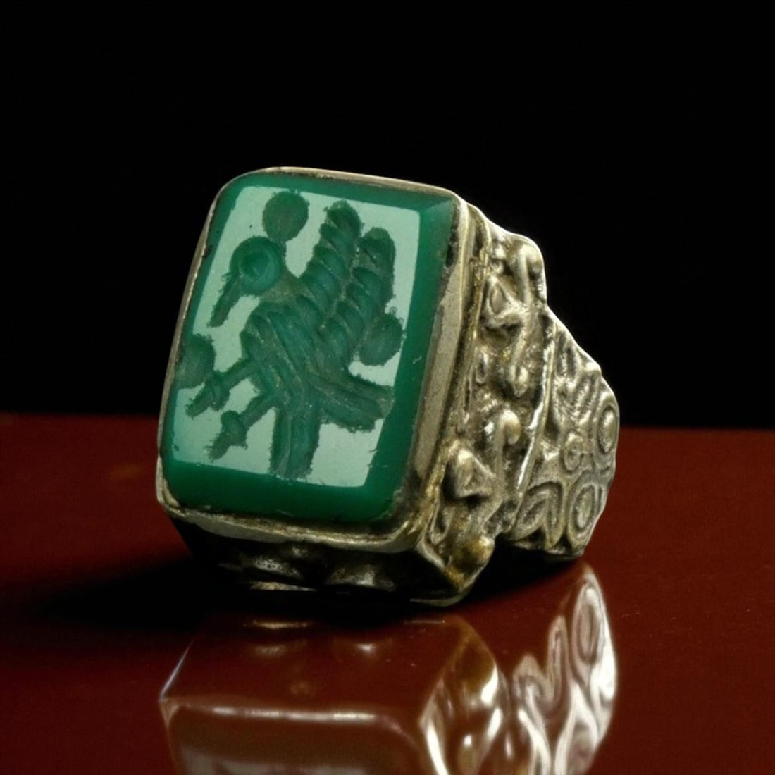 Ottoman Empire Silver Ring with Engraved Mythical Bird Motif, ca. 17th-18th Century: This substantial Ottoman silver ring exhibits finely detailed craftsmanship typical of the imperial courtly aesthetic. The centerpiece of the ring is a rectangular green hardstone, possibly chrysopras