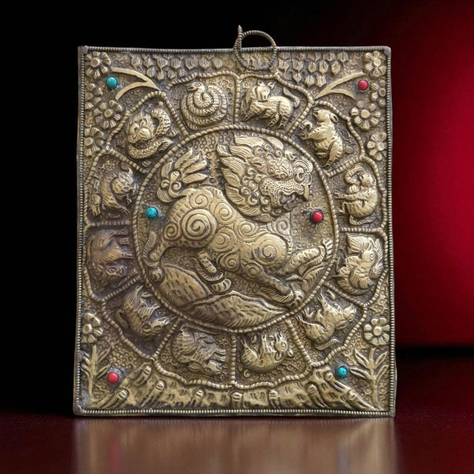 Tibetan Brass Wall Plaque with Zodiac and Fu Lion, 20th Century: This Tibetan wall plaque, crafted in the late 20th century, is made of repoussé brass with inset colored glass beads that enhance its decorative appeal. Measuring 19 by 22 cm and weighing 366 grams,