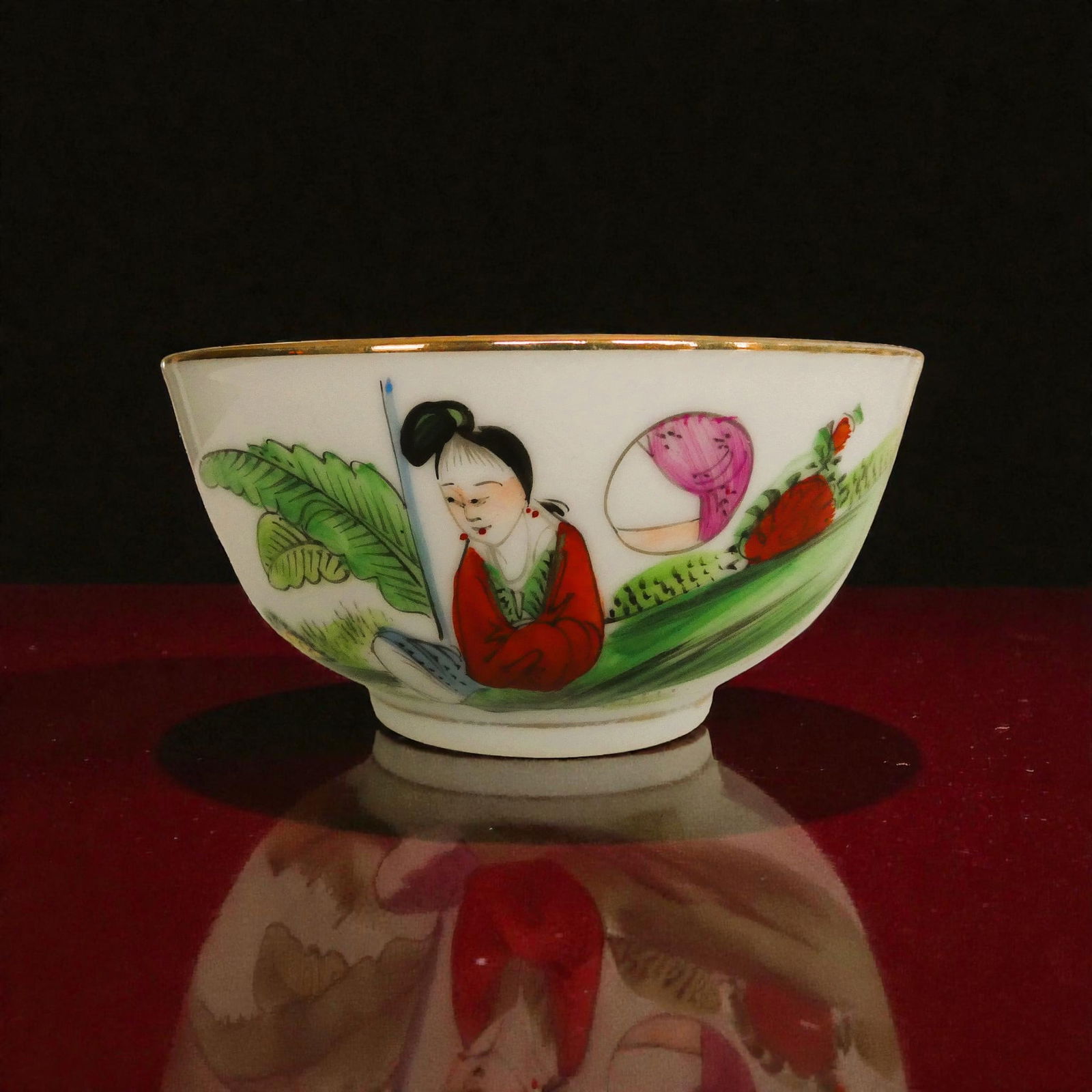 Chinese porcelain bowl hand painted figure scene gold rim 1950: This hand painted Chinese porcelain bowl dates to the mid 20th century circa 1945 to 1960 and shows a graceful figure scene set in a garden landscape with vivid greens, pinks and red tones enhanced by