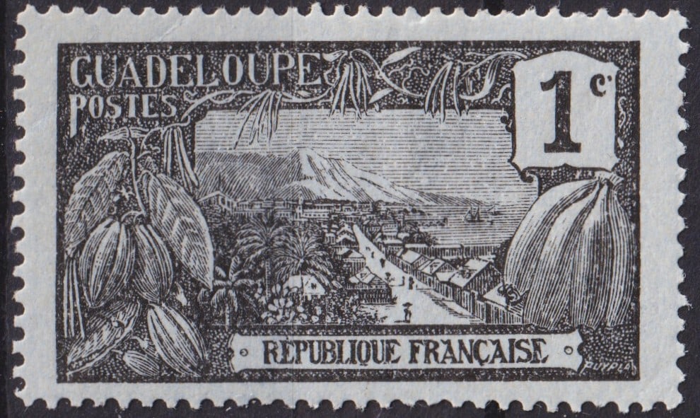 French Guadeloupe 1905 1c Black Landscape Issue Scott #61: This rare 1905 definitive stamp from Guadeloupe, denominated 1 centime in black, presents a striking engraved view of the island’s lush landscape with cocoa pods in the foreground, a picturesque har