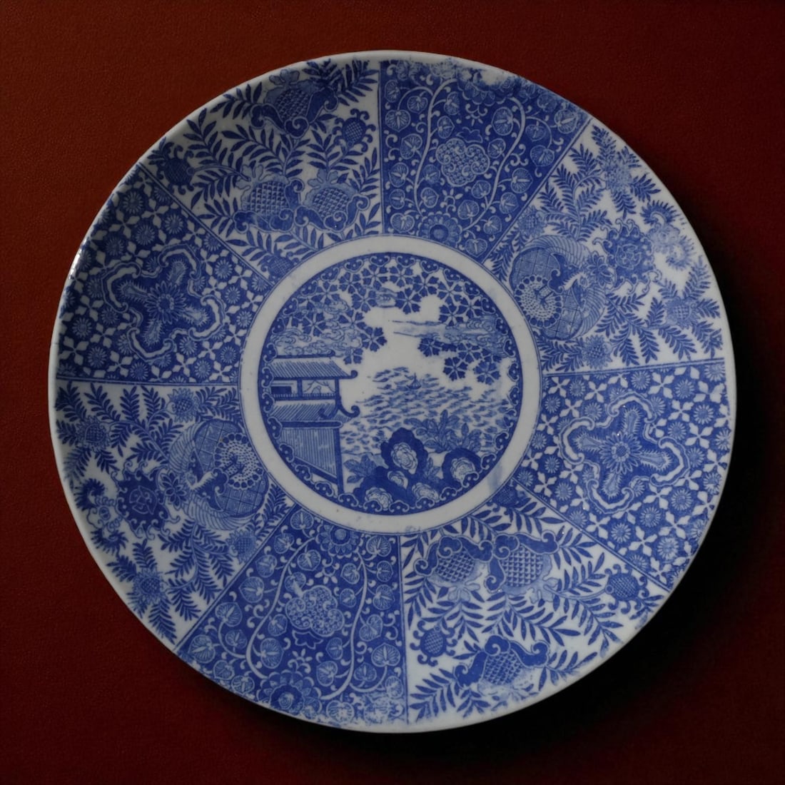 Large 19th Century Blue and White Porcelain Charger with Landscape and Floral Panels: This large blue and white porcelain charger, measuring an impressive 40.5 cm in diameter, represents a refined example of 19th-century export porcelain influenced by earlier Kangxi-period aesthetics. 