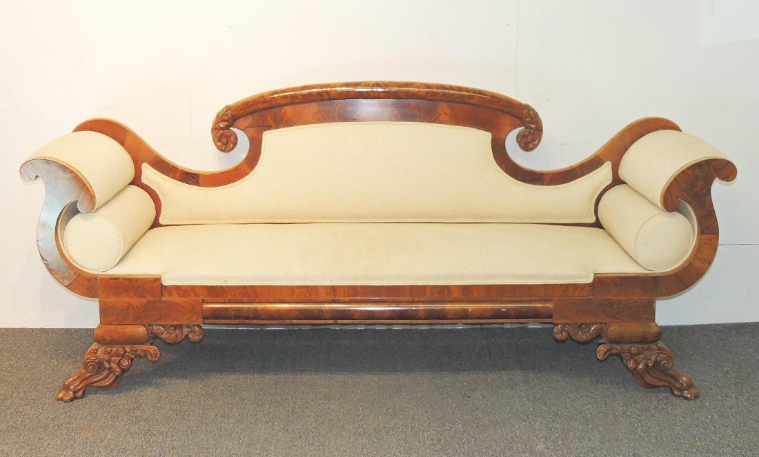 Empire Carved Mahogany Sofa: An Empire carved mahogany sofa with scrolled crest and arms on paw feet. Bolster cushions.