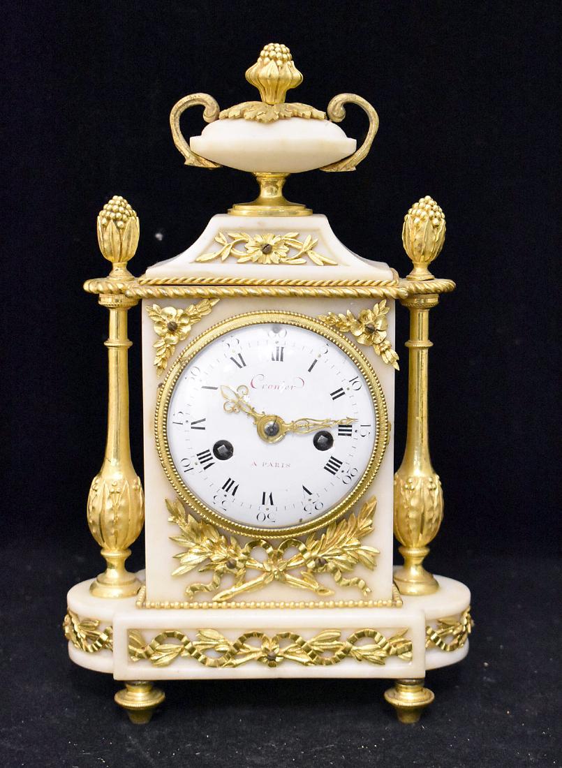 Louis XVI White Marble Mantel Clock: A Louis XVI white marble mantel clock with ormolu mounted case decorated with a ribbon and foliate motif, and having an urn finial flanked by gilt columns with pineapple finials. Porcelain dial signed