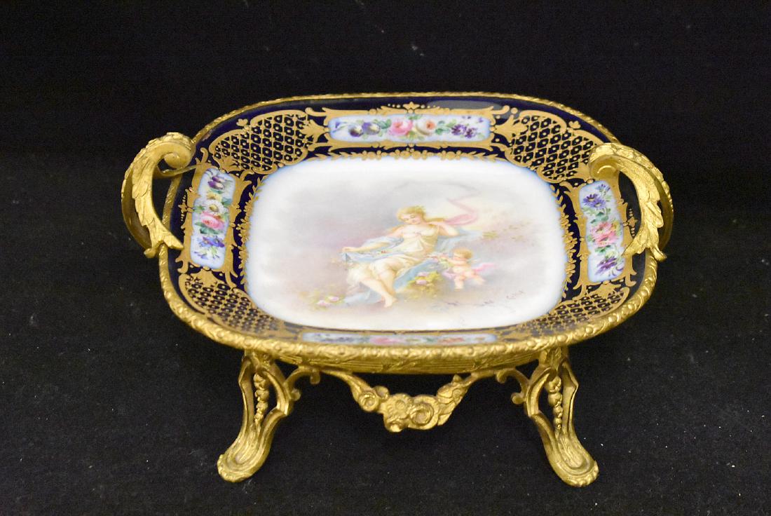 Sevres Porcelain Tray with Ormolu Mounts: A Sèvres hand-painted porcelain tray depicting a woman with cherub surrounded by a cobalt border with gilt accents and floral panels, signed "Cullot". Mounted in ormolu with acanthus handles an