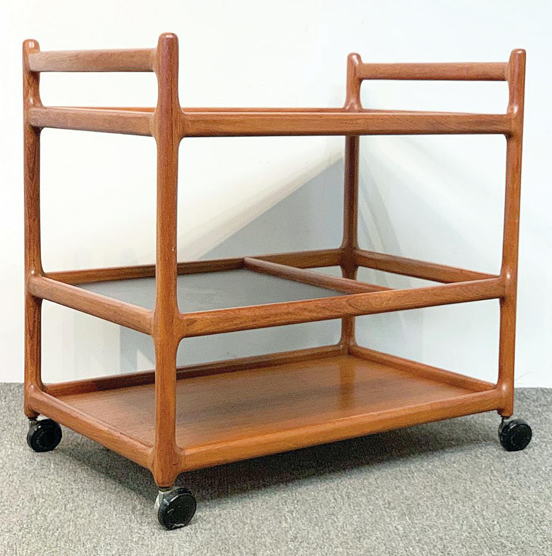 Johannes Andersen Teak Bar Cart: A Johannes Andersen for CFC, Silkeborg, Danish teak bar cart trolley with sculpted teak three-tiered frame and middle black laminate shelf, on casters. With metal medallion. 27-1/2in tall x 28in wide