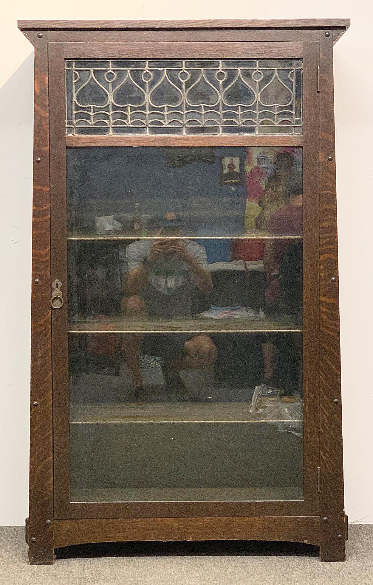 Limbert Arts & Crafts Oak Bookcase: A Limbert Arts & Crafts period oak bookcase with a rare tapered form, through-tenon construction, and single door with upper leaded-glass foliate panel. Marked 318 on back. 54in tall x 33in wide x 14-