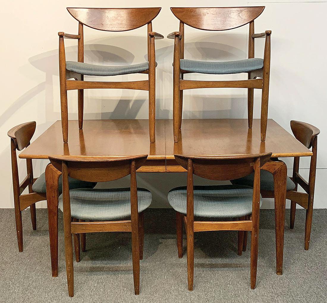 American Modern Dining Room Suite: An American modern walnut dining table with six chairs. Table with exposed frame and tapering legs and extra leaf. Chairs with shaped backs. Unmarked. Table: 29in tall x 62in long x 42in deep.