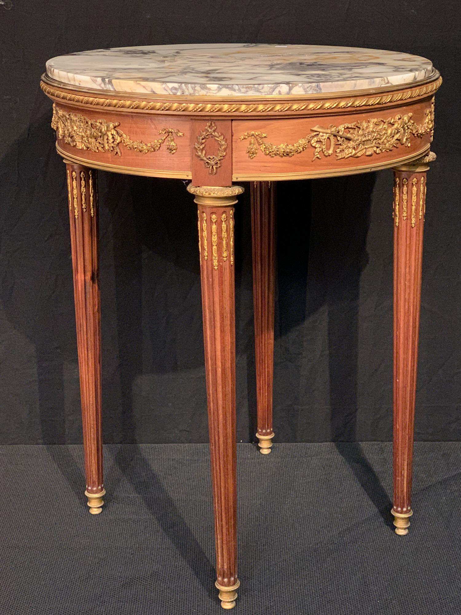 Louis XVI-style Marble-top Gueridon: A French Louis XVI-style mahogany gueridon, 19th/20th C., with a circular marble top, gilt ormolu mounts, and drawer in apron. 30in tall x 22-1/2in diameter.