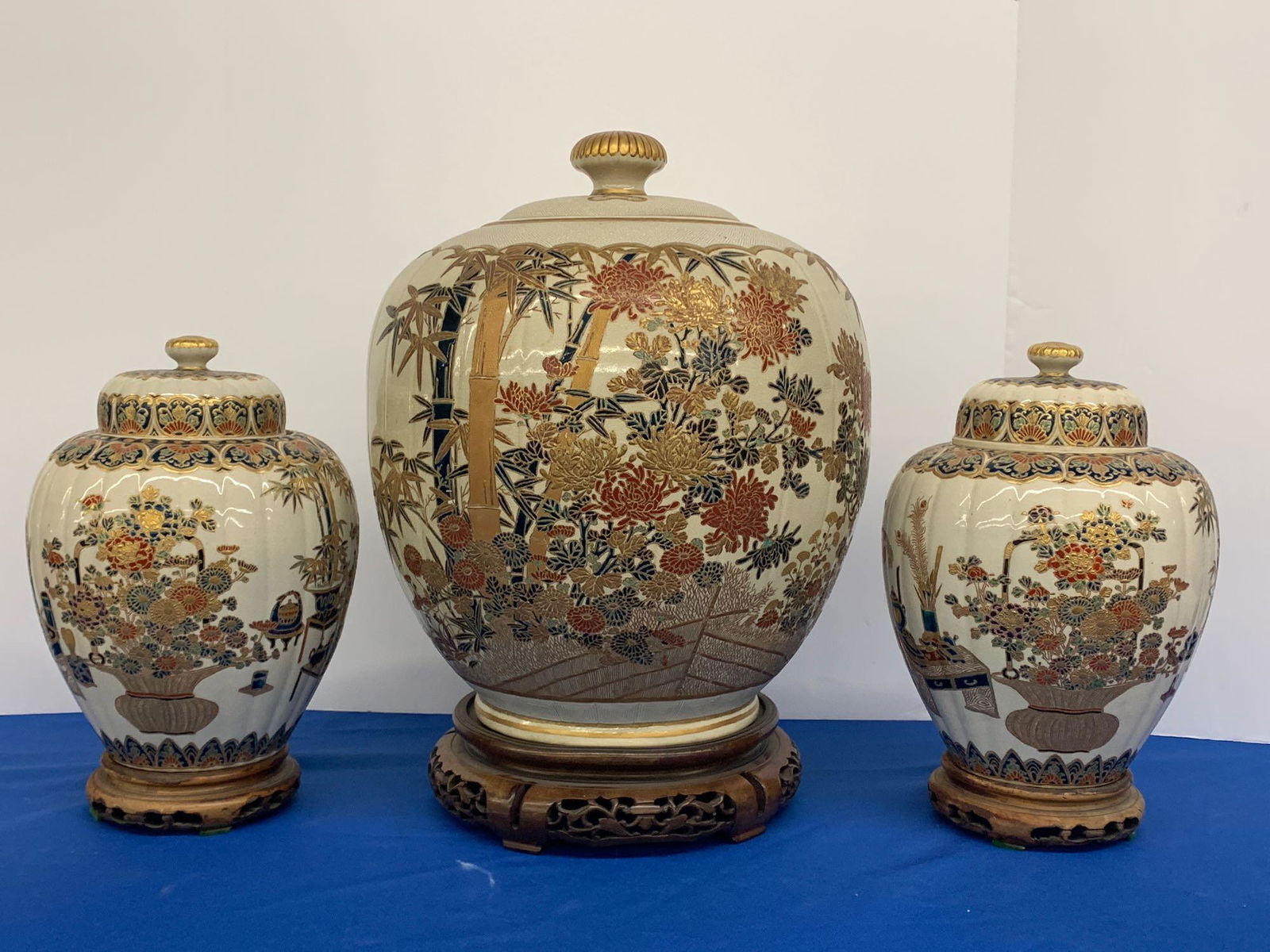 Fine, Large Japanese Satsuma Garniture Set: A fine and large Japanese Satsuma Shimazu garniture set comprised of a large Japanese porcelain koro or lidded jar with a blossoming tree and bamboo design, signed on base, and with hardwood stand; to