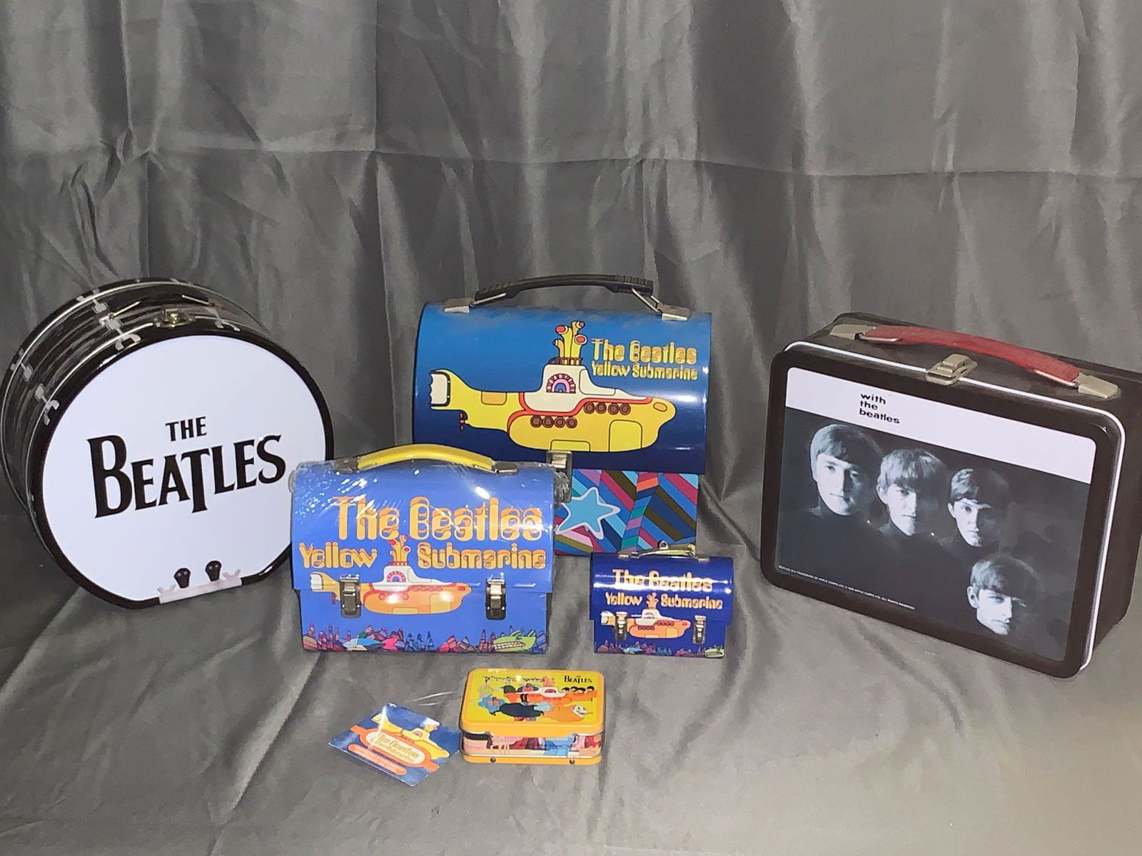 Grouping of Newer Beatles Lunchboxes: A grouping of newer Beatles lunchboxes including a drum, a "With the Beatles" album cover, and a "Yellow Submarine". Also, there is a Kurt Adler "Yellow Submarine " lunchbox ornament, a Hallmark "Yell