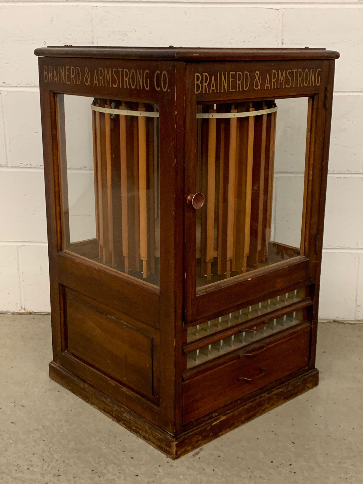 Brainerd & Armstrong Revolving Spool Cabinet: A country store countertop silk spool cabinet with gilt labeling on all four sides for Brainerd & Armstrong. The single door reveals a visible revolving display over three drawers, two with glass fron