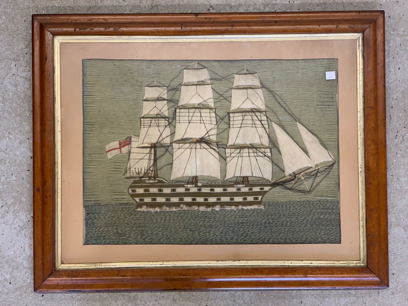 Needlework Woolie, British Ship at Sea: A 19th C. needlework woolie depicting a three-masted British ship at sea. Framed under glass in a period maple and gilt frame. Mat opening: 15-1/2in x 21-1/2in.