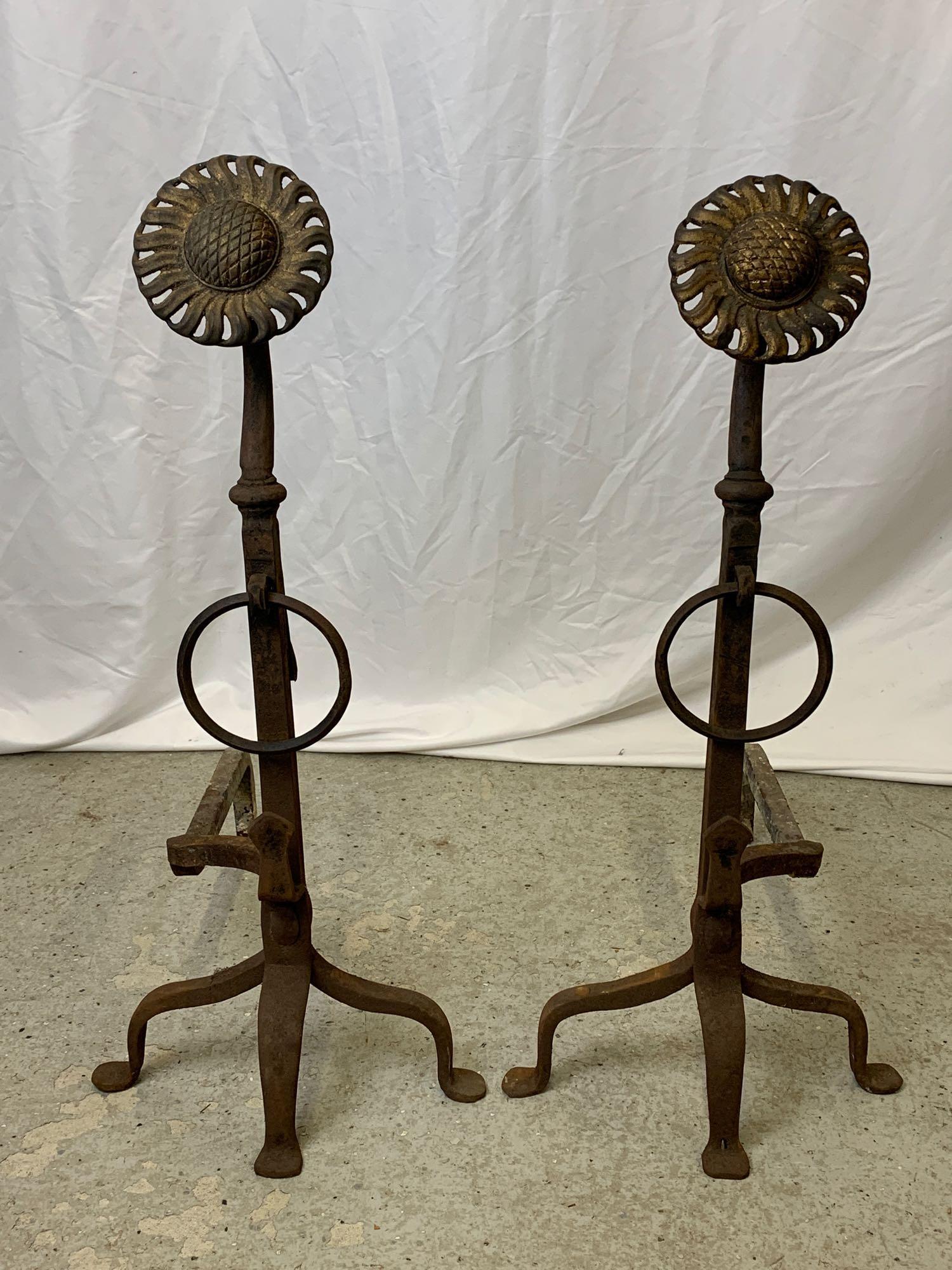 Pair of Aesthetic Sunflower Andirons: A pair of early 20th C. Aesthetic Movement wrought iron andirons with gilt sunflower finials. One appears to be signed STE(?) Each is 29 in tall x 13-1/2 in wide x 22 in deep.