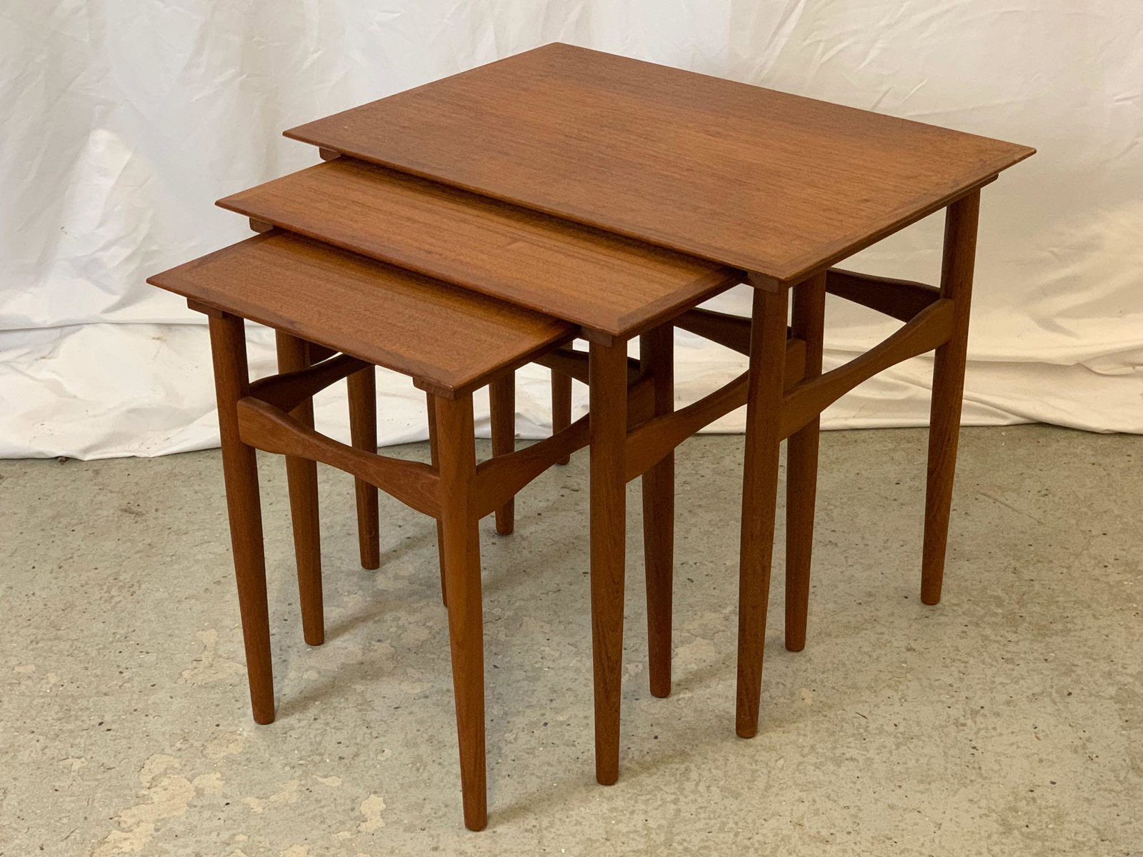 Nest of Three Danish Teak Side Tables: A nest of three Danish Modern teak side tables on tapering legs joined by sculpted stretchers. Largest table: 19 in tall x 23 in wide x 16 in deep.