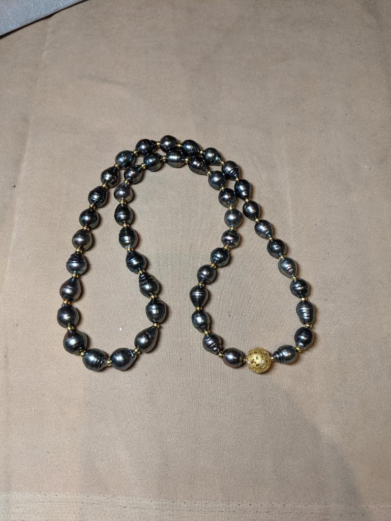 Strand of Black Pearls: A 26in strand of oblong black pearls in slightly graduated sizes up to 11mm diameter with gold bead spacers and spherical clasp with scattered diamond accents and cut-work.