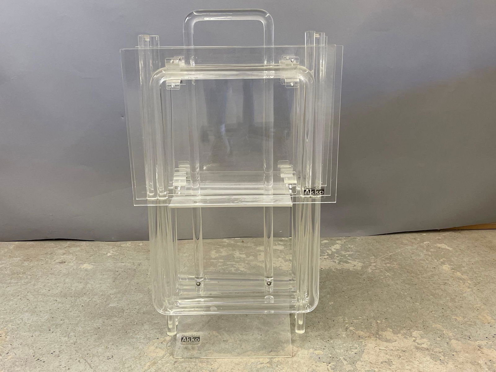 Four Akko Lucite Trays: A set of four Akko lucite folding trays with stand. Trays: 26-1/2in tall x 20in wide x 15in deep. Stand: 35in tall x 9-1/2in wide.