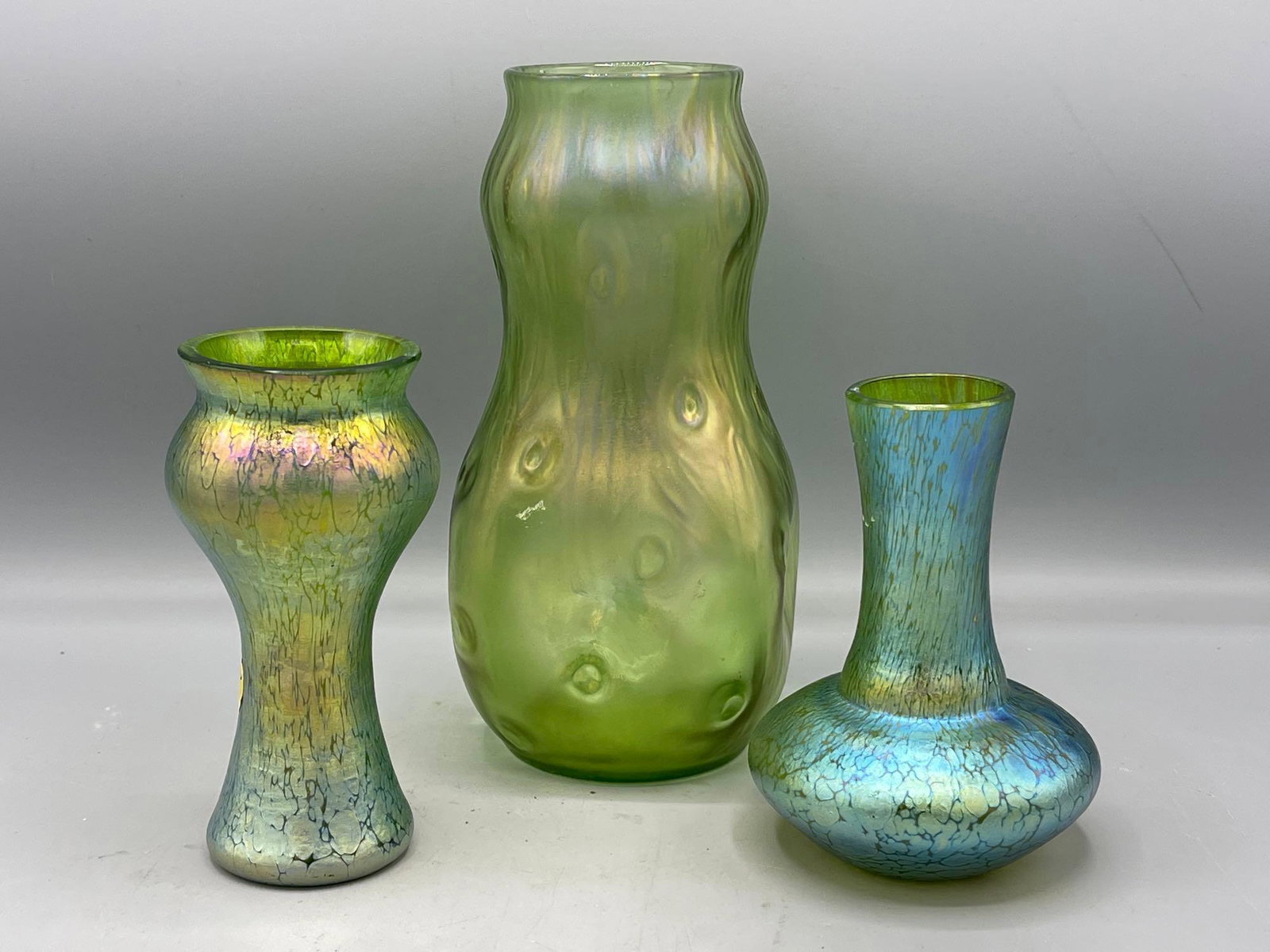 Three Loetz-style Favril Vases: A grouping of three Loetz-style vases including a large amorphous vase with iridescent favrile style glaze, and two petite opalescent vases. Largest: 8in tall.