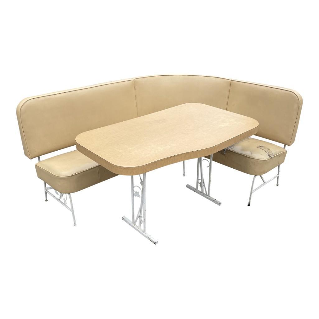 1950s Dinette Diner Style Corner Seating and Table: (R) A readymade corner dining nook complete with an L-shaped bench seat and ergonomic wooden table, both with wrought iron floral bases. The vinyl on the bench seat has two linear tears along the shor