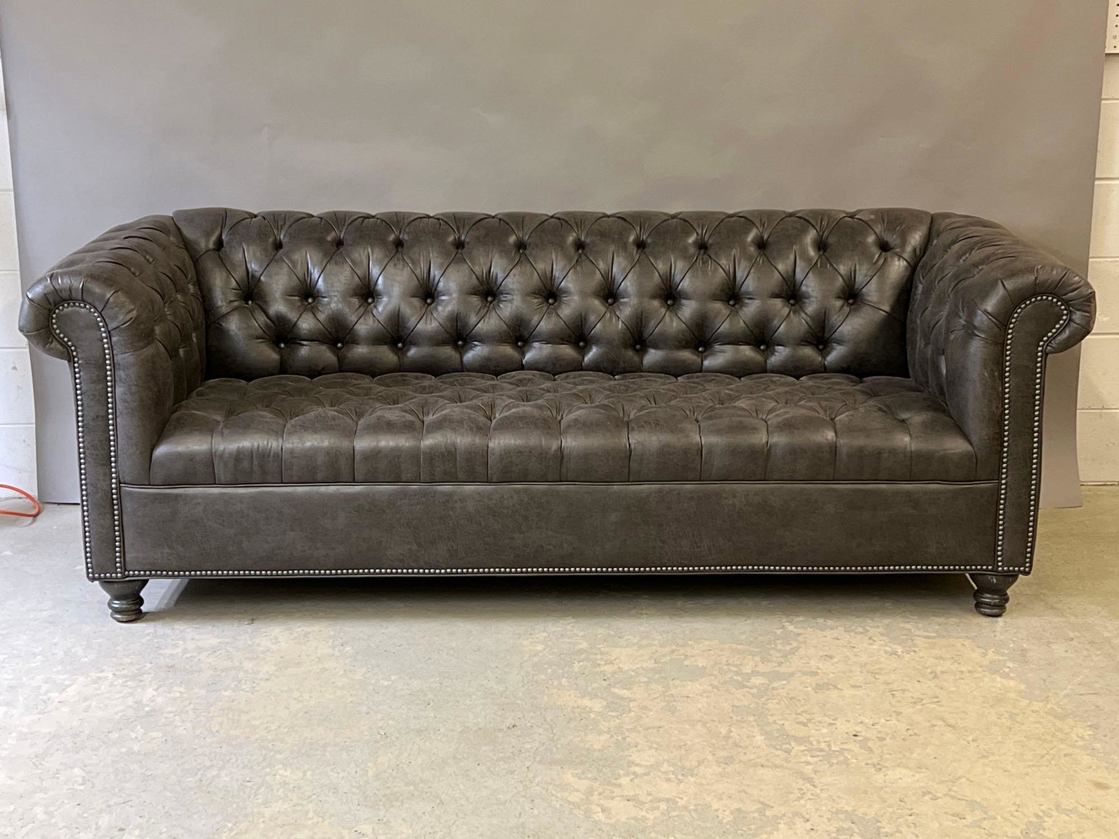 Decorator Chesterfield Sofa: A contemporary decorator grey chesterfield sofa with rolled arms and tacked trim. 30in tall x 86in wide x 36in deep. | Local and NYC curbside delivery details and international third-party shipper rec