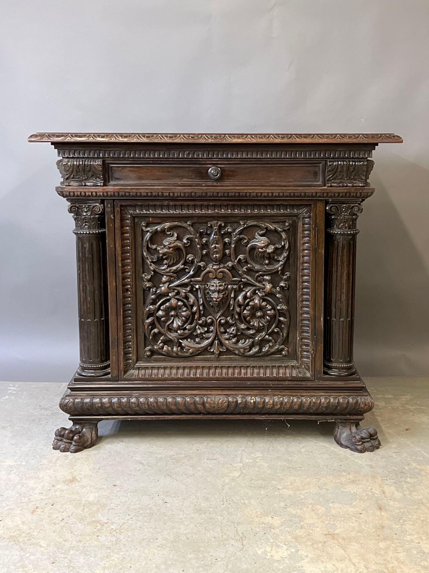 Renaissance Revival Carved Mahogany Cabinet: A 19th C. Renaissance Revival carved mahogany cabinet with a single drawer over a door, the front heavily carved with lions mask and dragons with scrolling vines and flowers, flanked by full columns, 