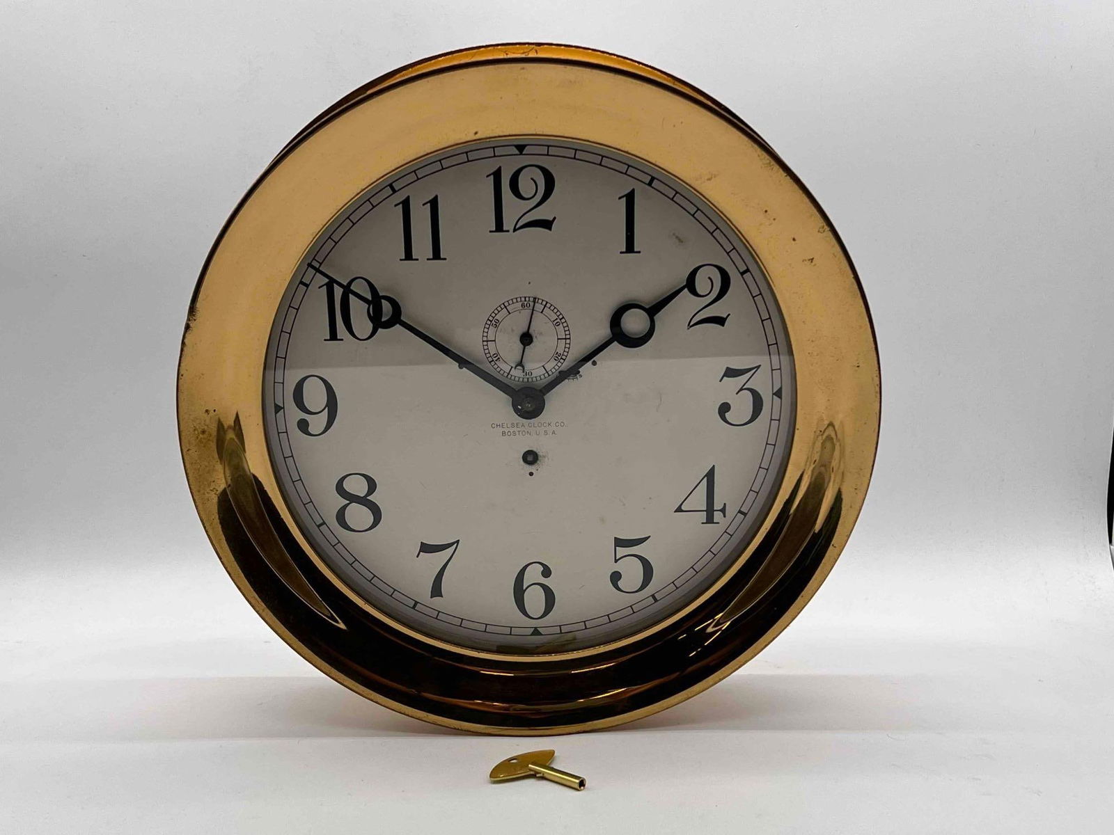 Chelsea 12-Inch Ship's Bell Wall Clock: A large Chelsea brass ship's bell wall clock, circa 1917, serial #106442, with a brass case and painted dial. Dial diameter: 12in. Full diameter: 14-1/2in. With certificates of origin from Chelsea Clo