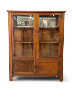 Stickley Brothers Two Door Oak China Cabinet: A Stickley Brothers two-door china cabinet or bookcase with a paneled back and interior mirror, over two paneled wooden doors, with original hardware. Quaint label on back. 60in tall x 49in wide x 15-