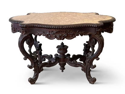 Victorian Caved Rosewood Parlor Table: An American Rococo Victorian carved rosewood parlor table with an inset marble top and scrolled legs joined by a stretcher and acanthus finial. 28in tall x 47in wide x 29in wide. | Philadelphia Metro