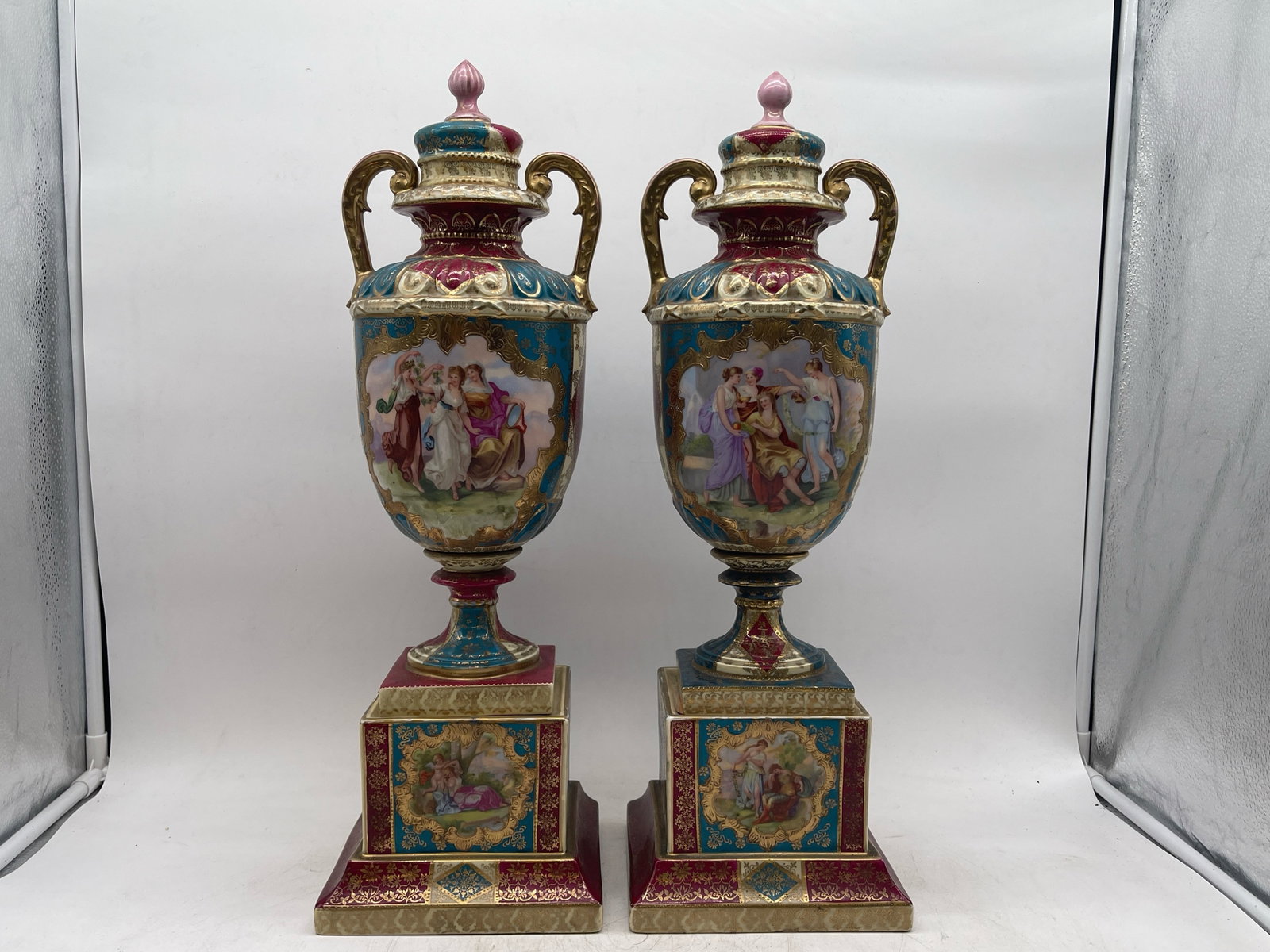 Pair of Royal Vienna Porcelain Lidded Urns: A pair of Royal Vienna porcelain lidded urns with classical Grecian scenes hand-painted at center, and gilt and floral decoration. Beehive mark on bottom. 21-1/2in tall x 7in wide. | Philadelphia Metr