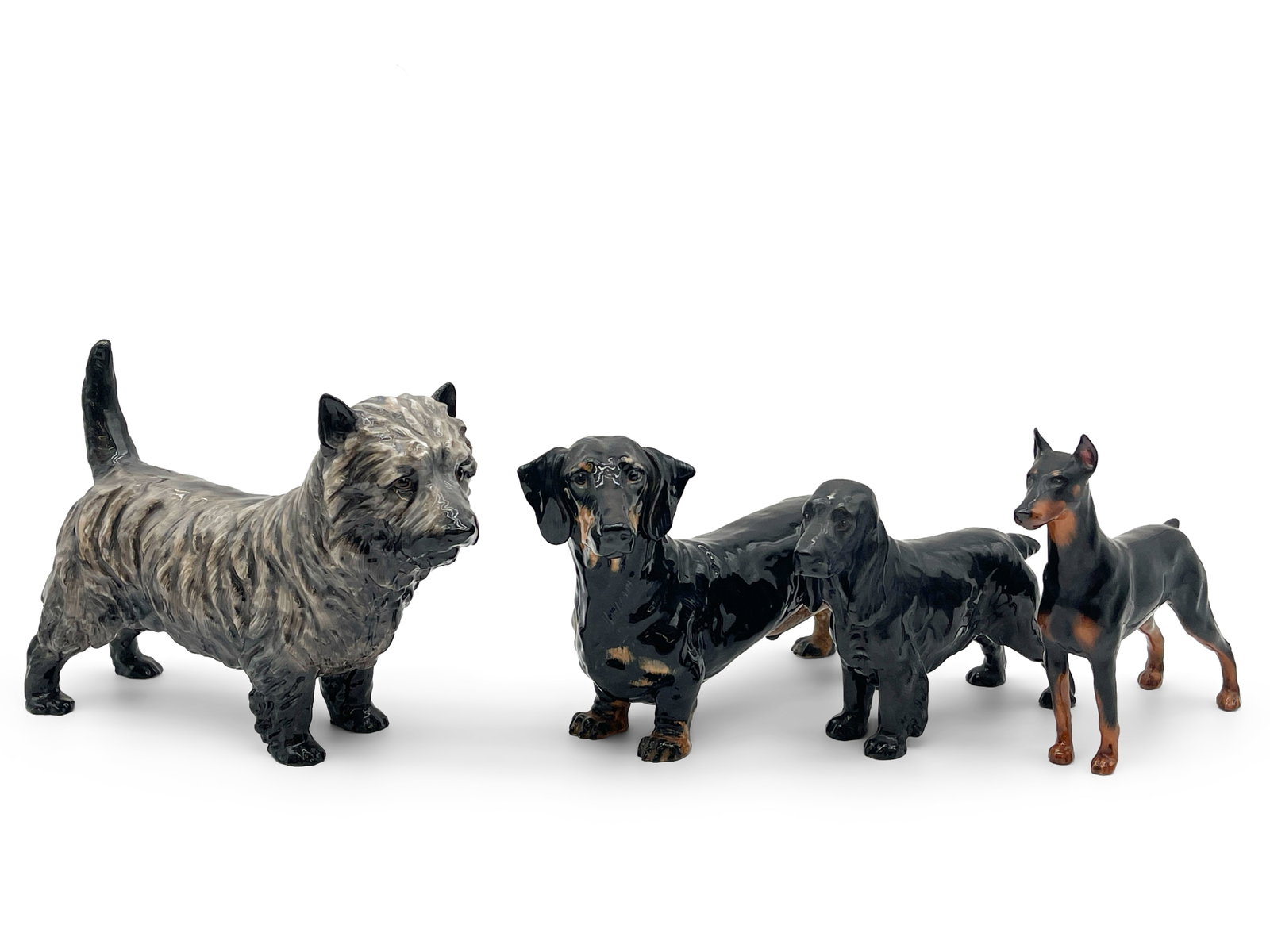 Four Royal Doulton Dog Figurines: Four Royal Doulton bone china dog figurines: a Rancho Dobe's Storm Doberman, Charming Eyes cairn terrier, a black spaniel, and a dachshund. All marked on back paw. Largest: 7in tall x 8in wide. | Phil