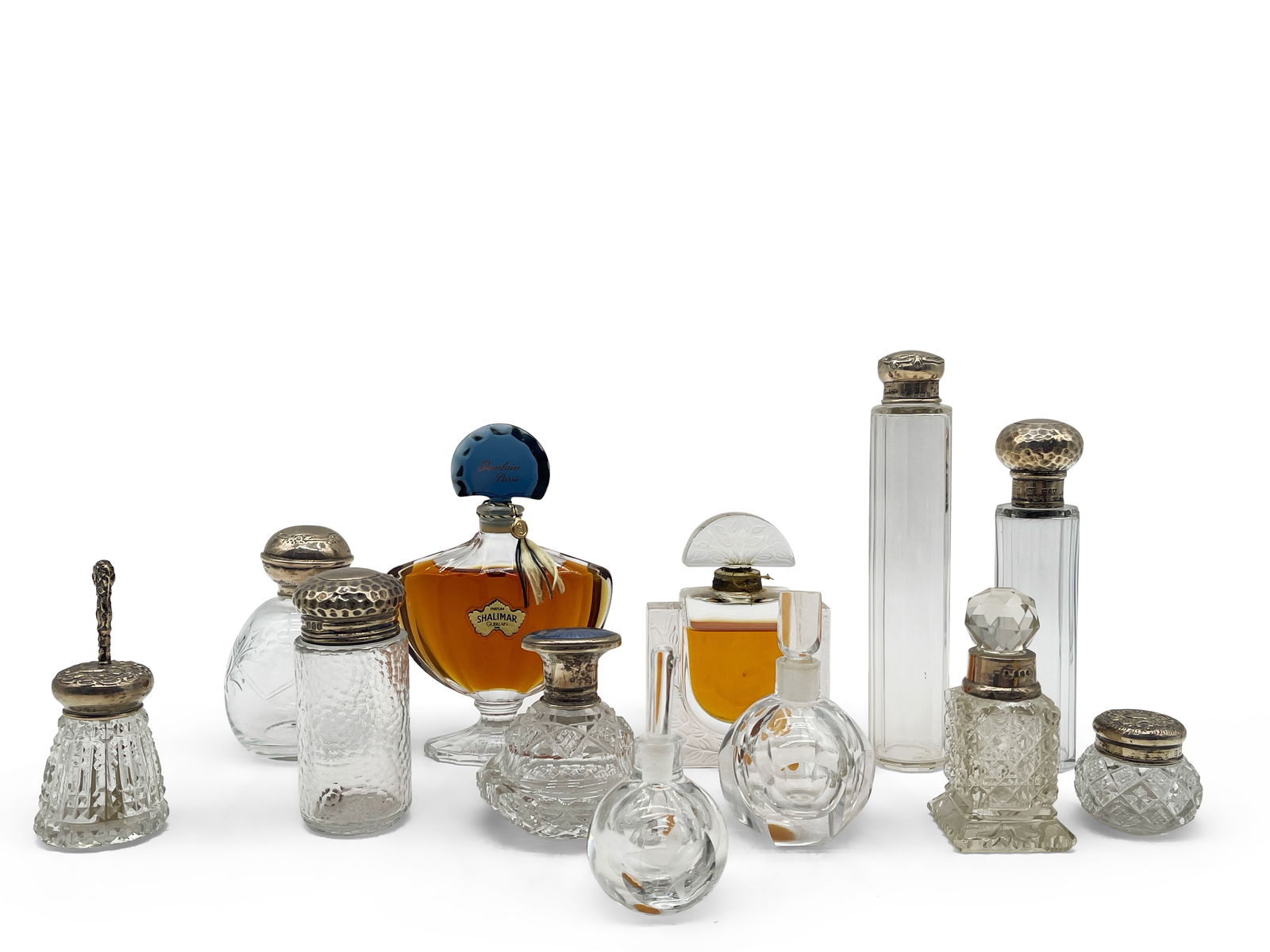 12 Designer and Other Perfume Bottles: A grouping of 12 perfume bottles to include Shalimar by Guerlain, a bottle of Lalique, two signed art glass bottles, and eight sterling-lidded cut glass bottles. Largest: 7-1/2in tall. | Philadelphia
