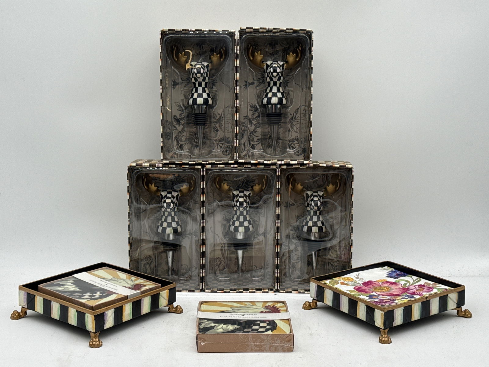 MacKenzie-Childs Moose Bottle Stoppers and Coasters: Five MacKenzie-Childs moose form bottle stoppers in original packaging, two paw foot napkin stands, and two Sunrise cork back coasters in original packages. Each marked MacKenzie-Childs. Boxes: 7in ta