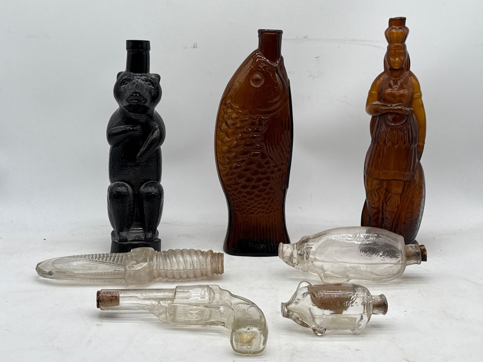 Seven Figural Glass Flasks or Bottles: Seven figural bottles or flasks to include W.H. Ware Fish bitters; 1867 Brown's Indian Herb Bitters; a glass bear flask; knife-form flask; gun-form corked flask; a Good Hal Bourbon corked pig; and a p
