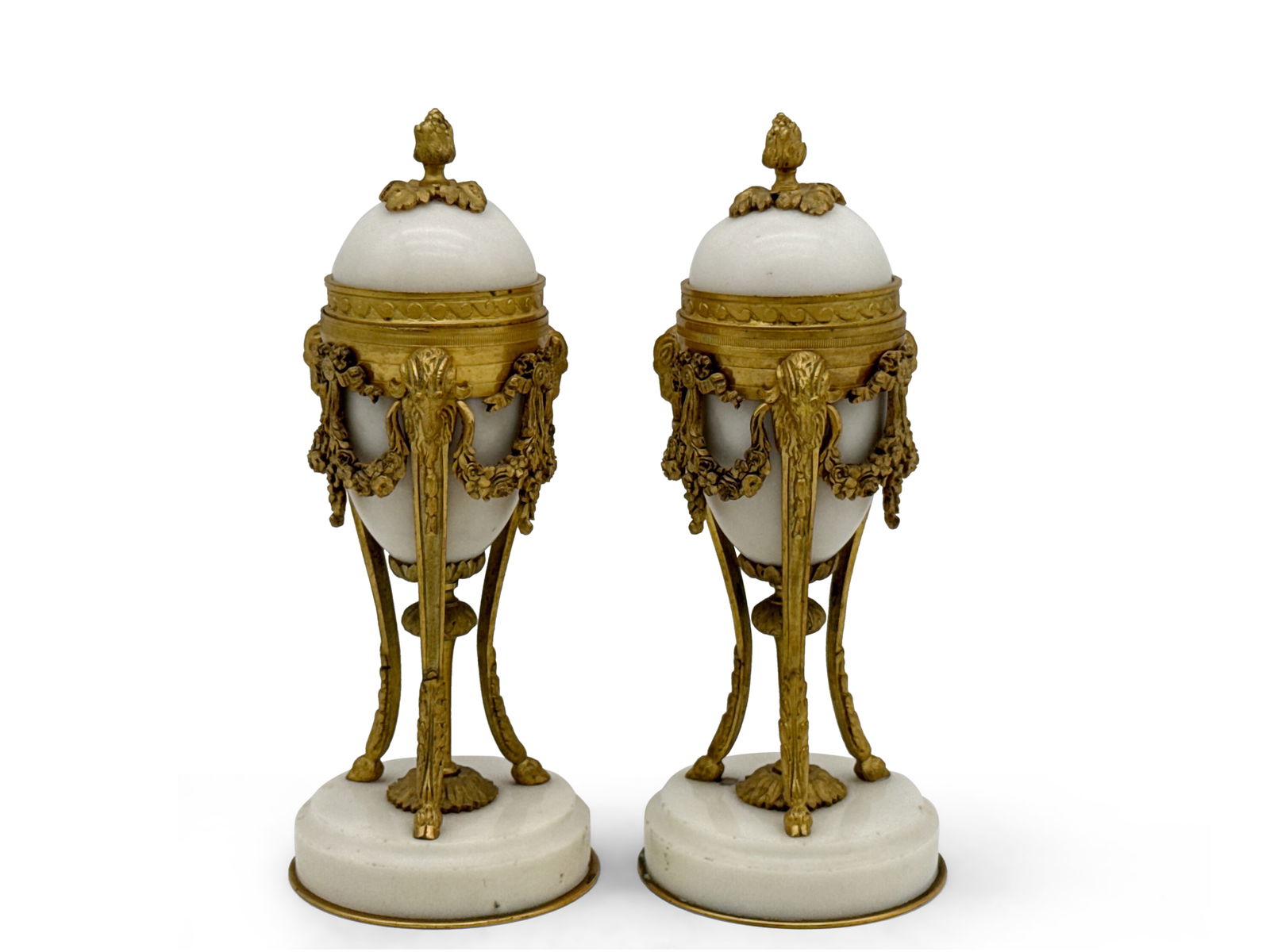 Pair of Louis XVI Style Gilt-Bronze and Marble Cassolettes: A pair of Louis XVI-style gilt bronze and white marble cassolettes, having lids with berried finials reversing to candle holders, raised on trefoil legs surmounted with ram's masks and terminating wit