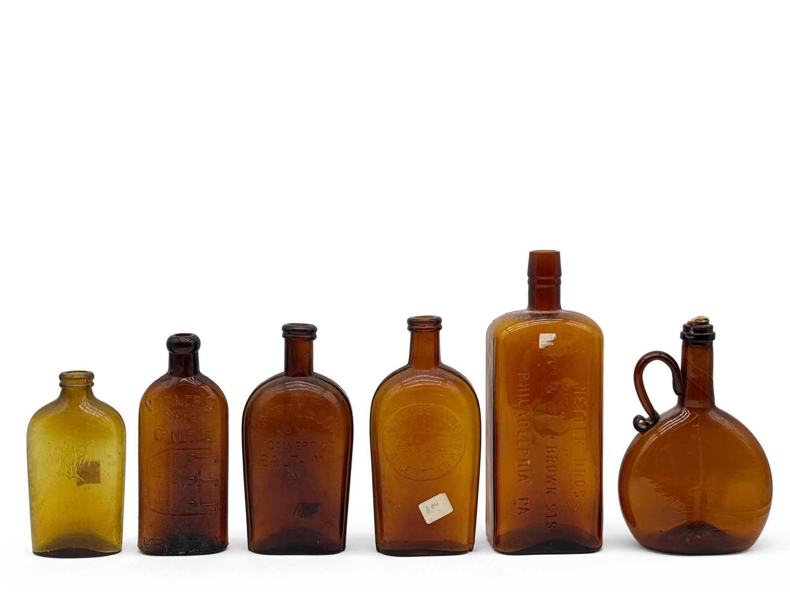 Six 19th C. Amber Glass Whiskey & Apothecary Bottles: Grouping to include an olive glass eagle flask, a Warner's Cure apothecary bottle, an R. McRae & Son Baltimore flask, a Charles Kline Allentown flask, a Netter Bros Philadelphia flask, and an amber ch