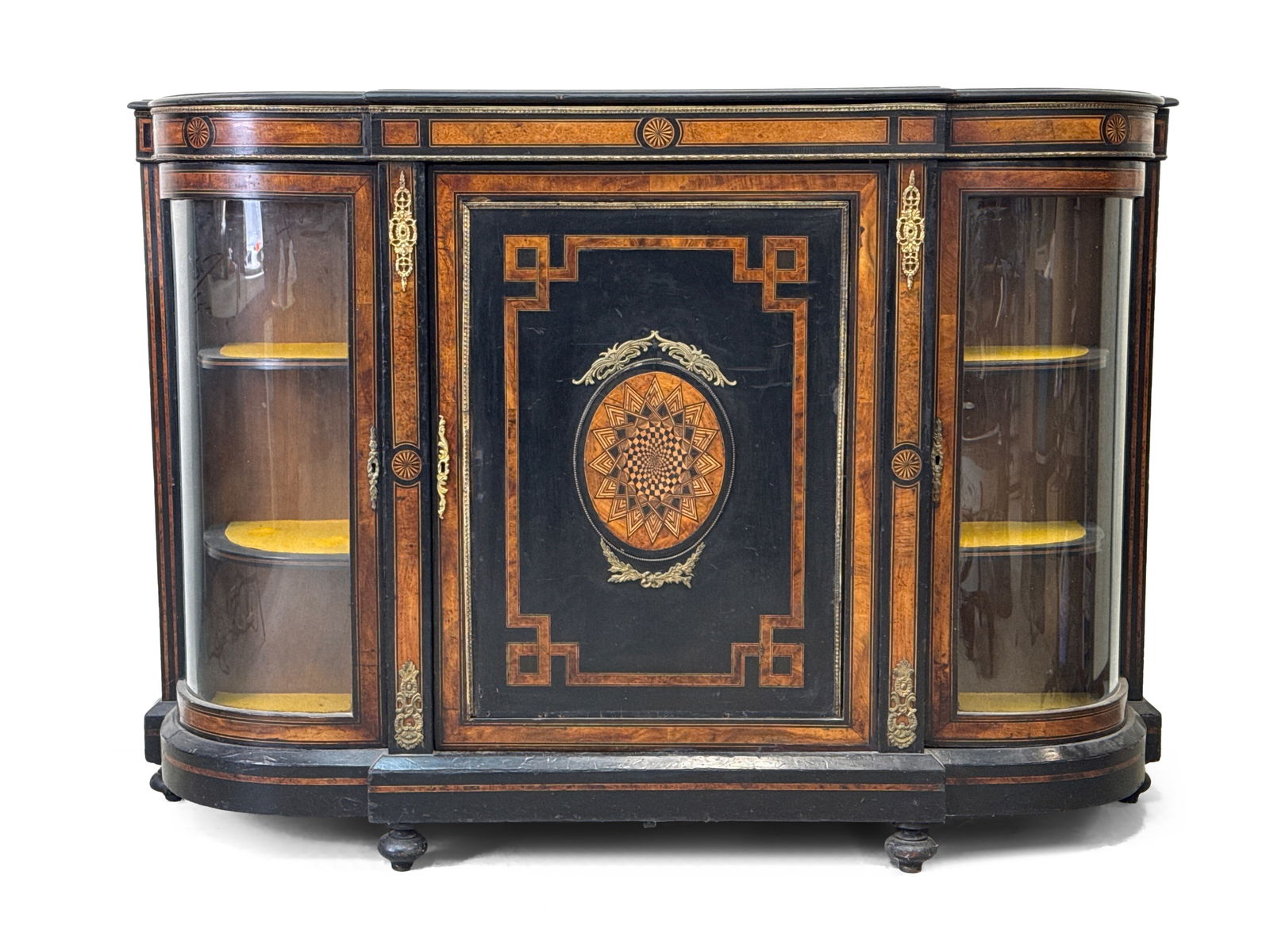 Victorian Ebonized and Amboyna Credenza: A Victorian credenza with an ebonized top above a frame with inlaid amboyna banding through the central door with a bold oval panel in an ormolu frame, flanked by bowed glazed doors, raised on short b